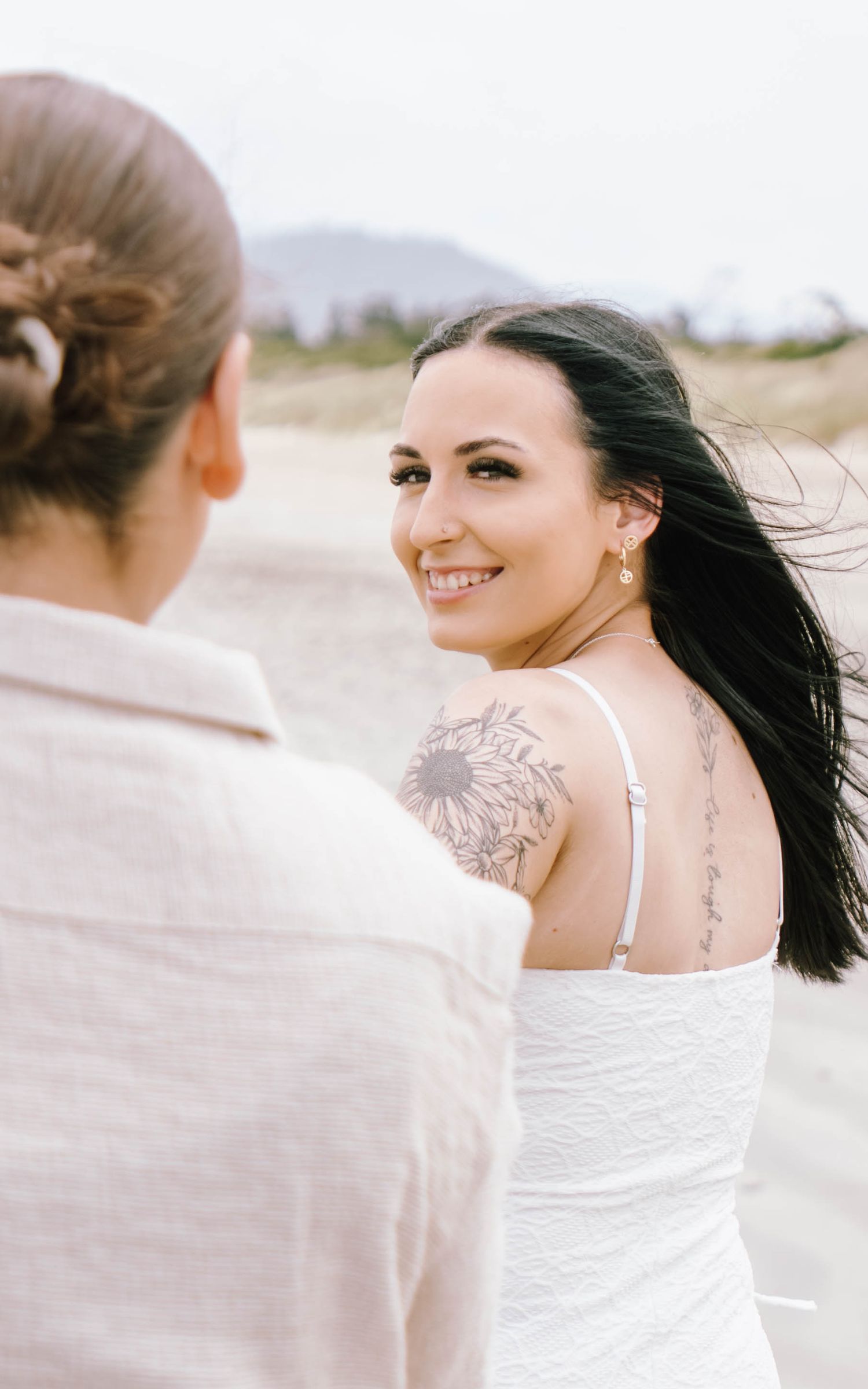 Woman in white dress smiling and enjoying a breezy moment at the beach with her hair flowing in the wind.