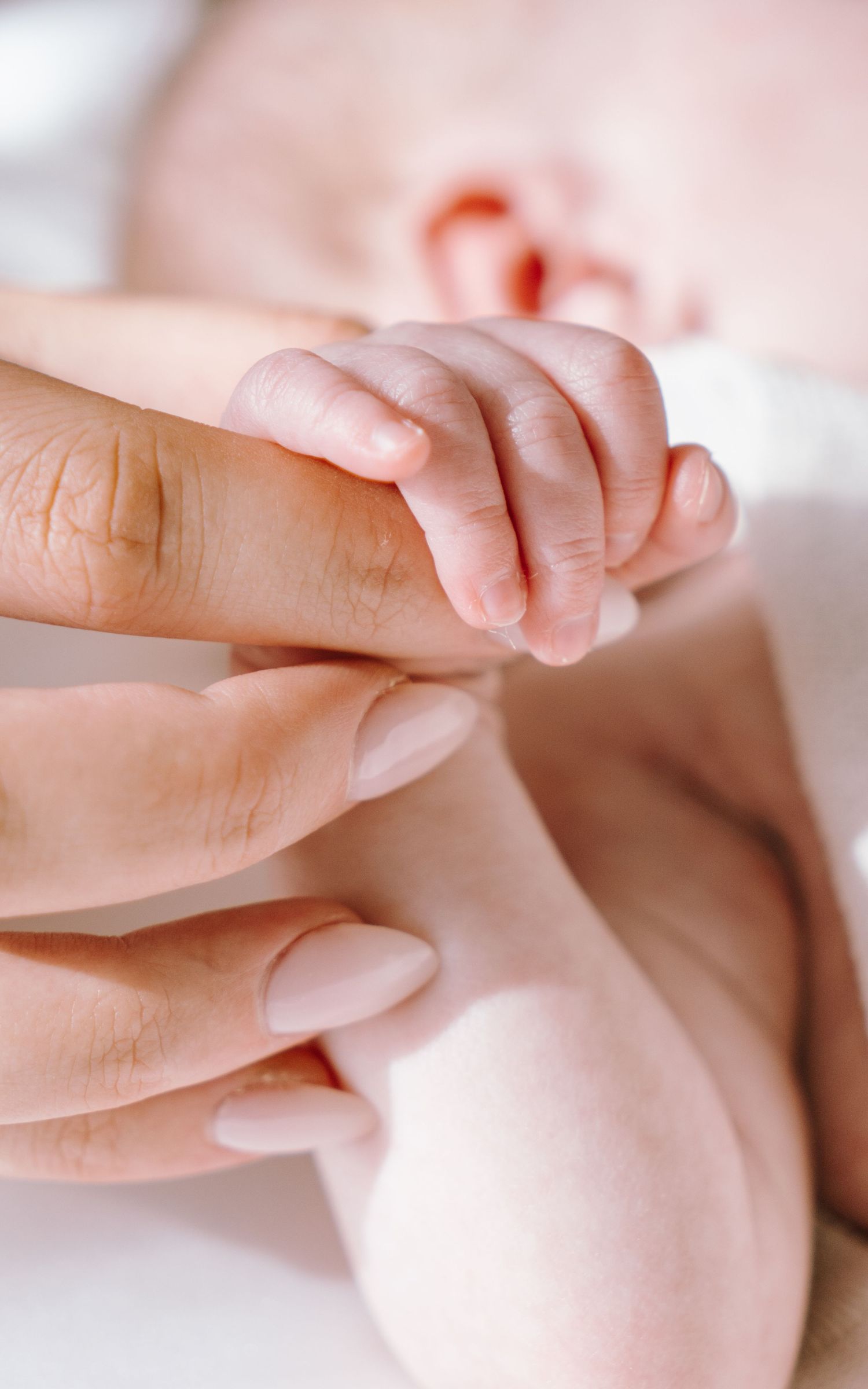A close-up series of baby hands grasping and touching adult fingers against a soft pink background.