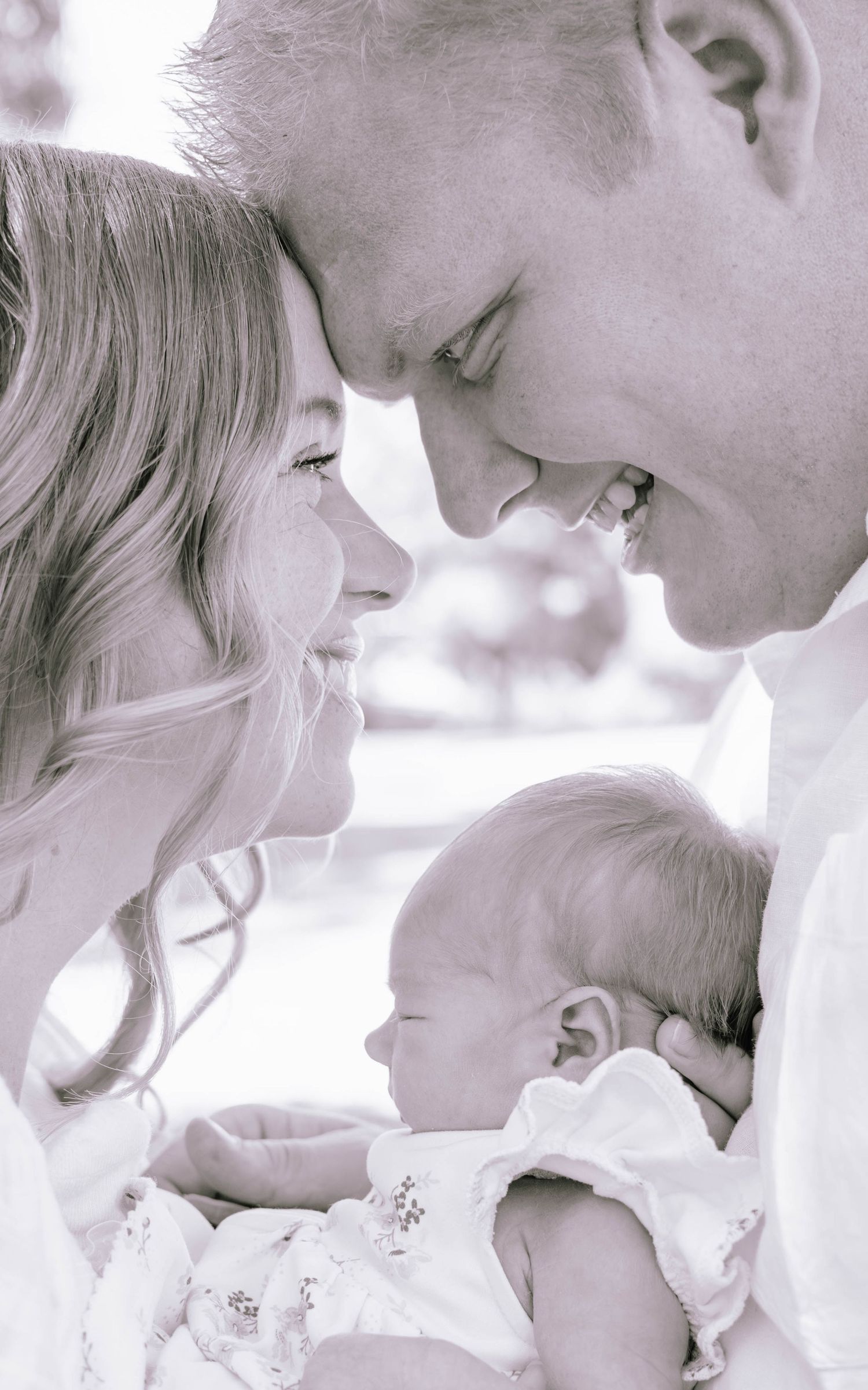 Black and white photo of loving parents smiling at their newborn baby held between them.