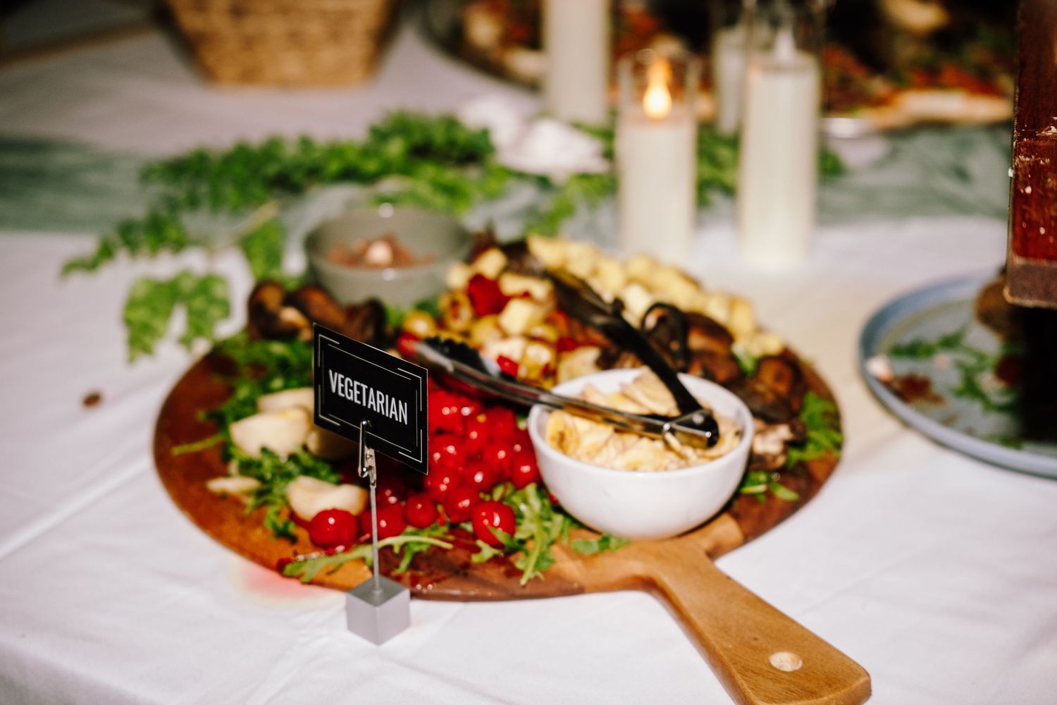Vegetarian charcuterie board with fresh greens, tomatoes, and dips on a wooden paddle at an elegant event.