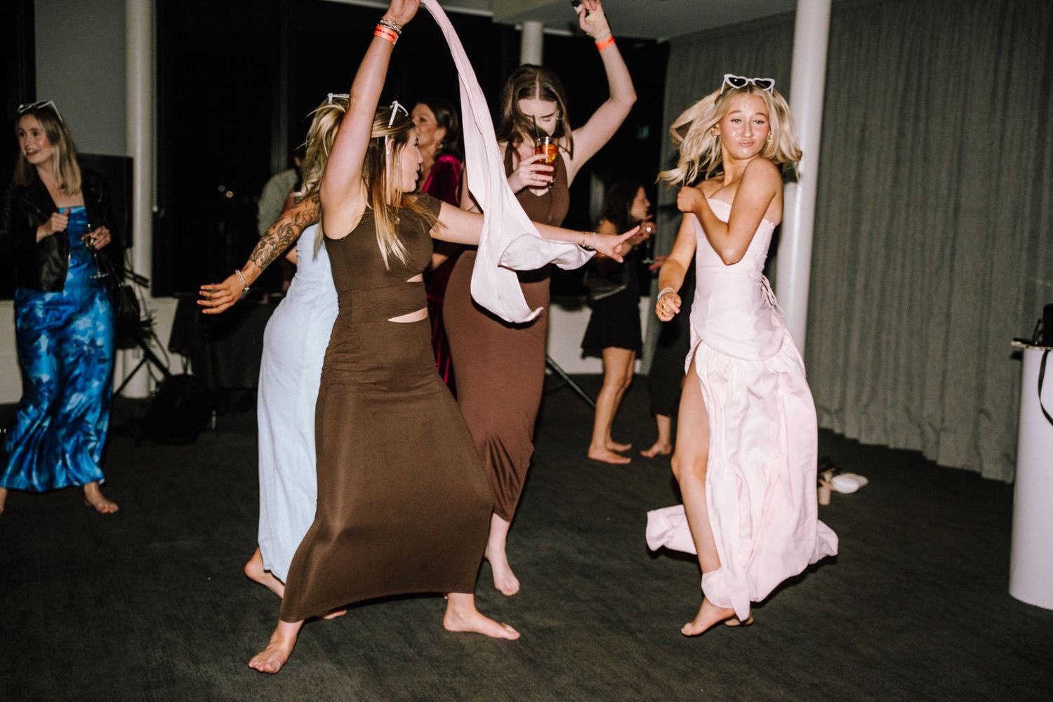 Women in elegant dresses dancing barefoot at a wedding reception party.