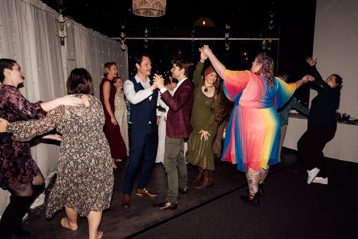 Group of people dancing joyfully at an indoor party, with colorful outfits and festive atmosphere.