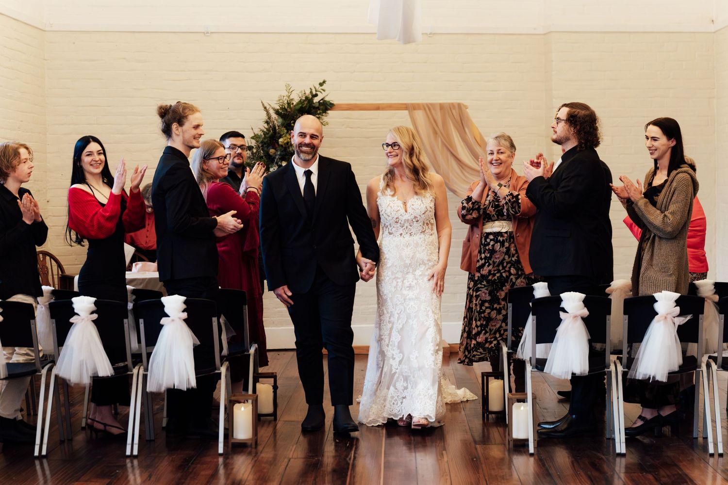Newlywed couple walks down the aisle hand in hand as guests applaud at an elegant indoor wedding ceremony.