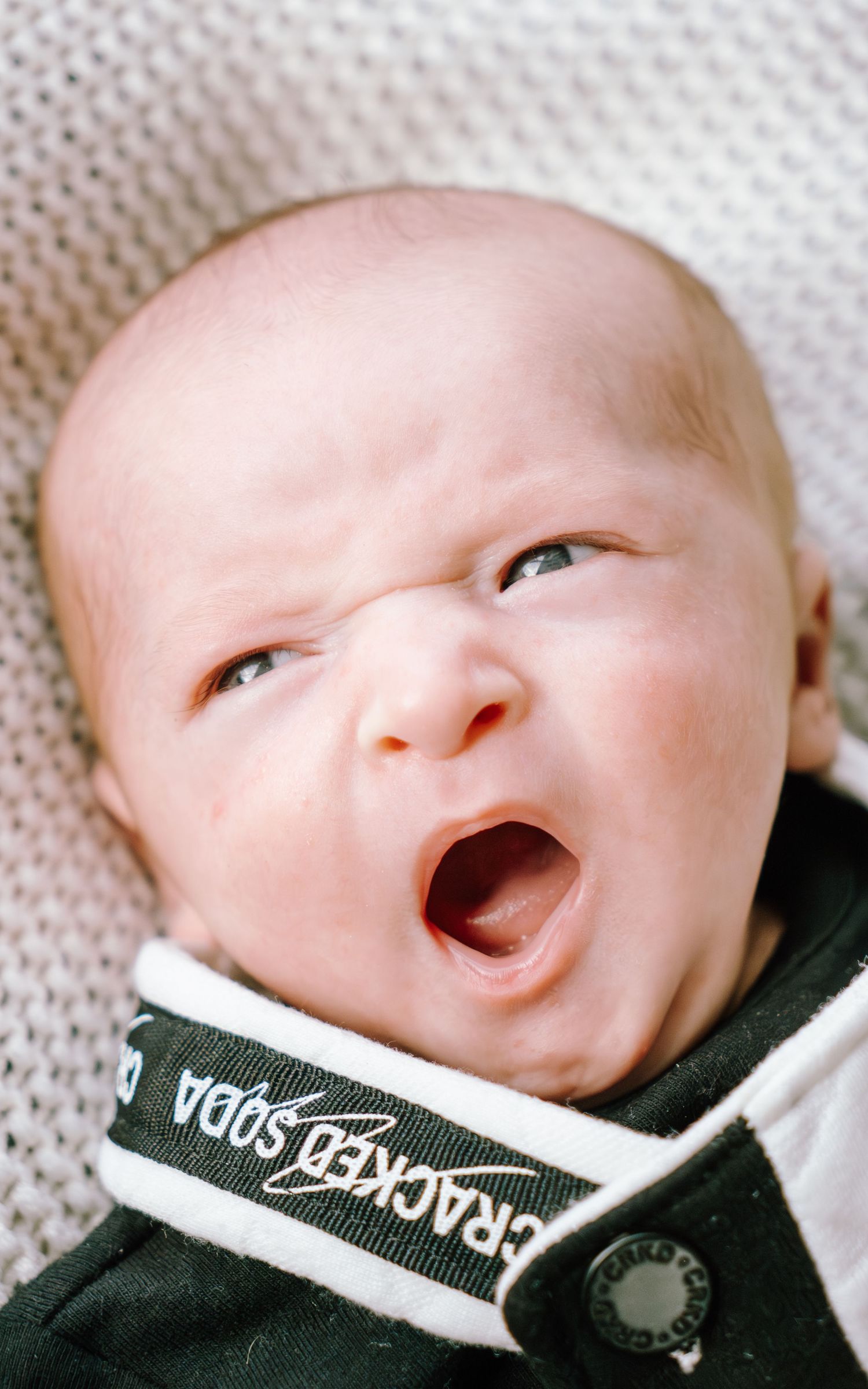 A series of close-up photos showing a baby yawning while wearing a dark colored garment with white trim.