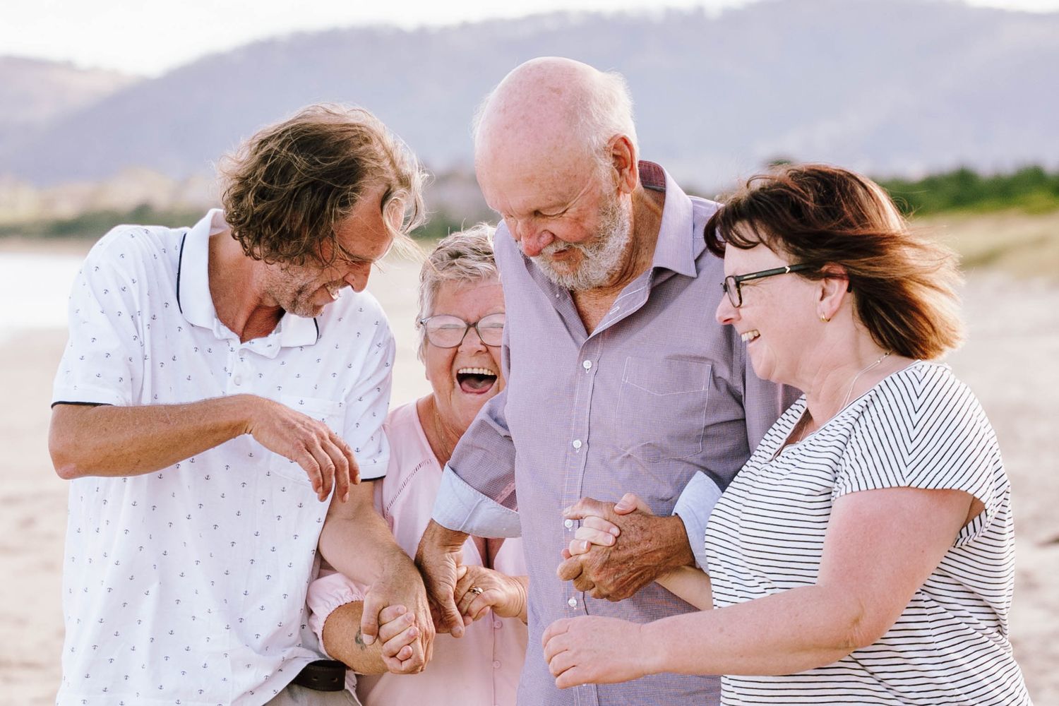 Happy multigenerational family laughing together on a sunny beach, sharing a joyful moment outdoors.
