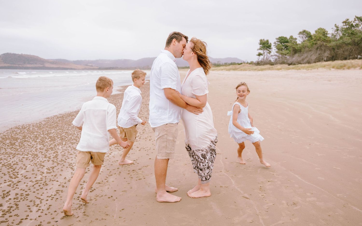 Candid family photos taken along a peaceful coastal beach with mountains in the background.