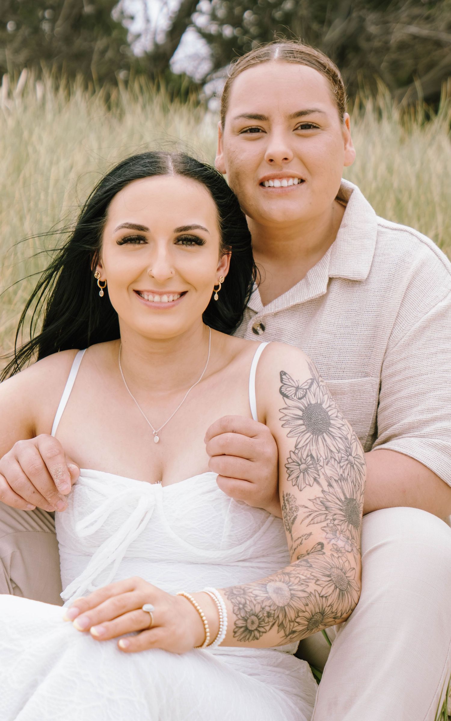 Couple in white outfits embracing outdoors in a field of tall grass during a photo session.