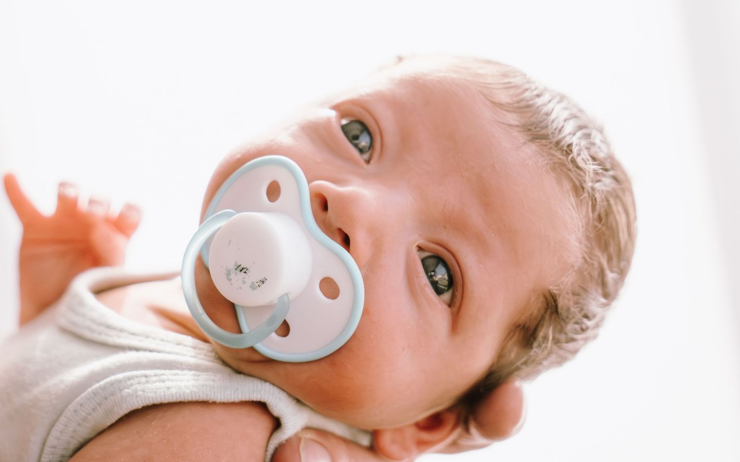 Baby lying down with a pacifier in their mouth shown from three different angles.