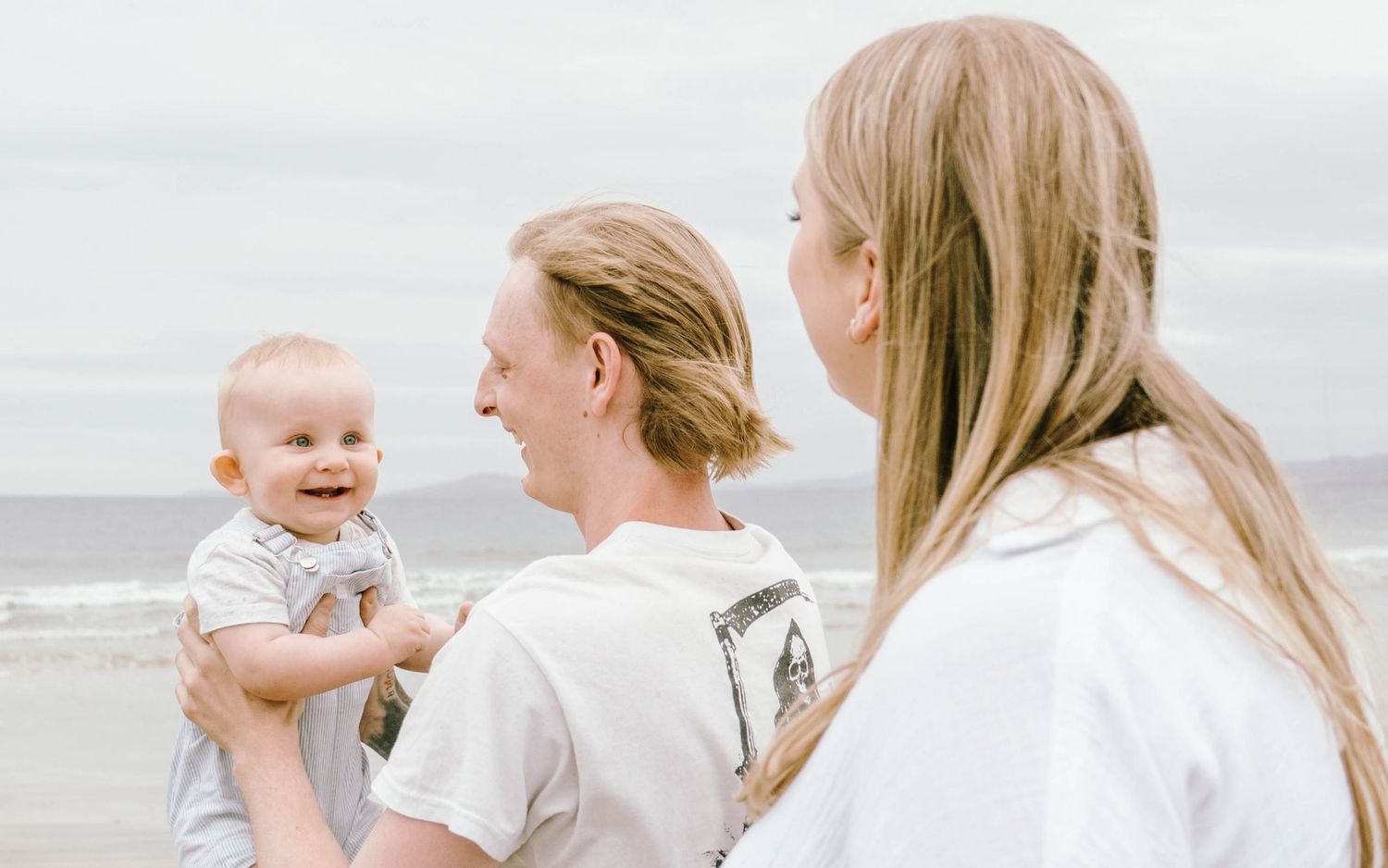 A series of candid beach photos showing tender moments between family members on a cloudy day by the ocean.