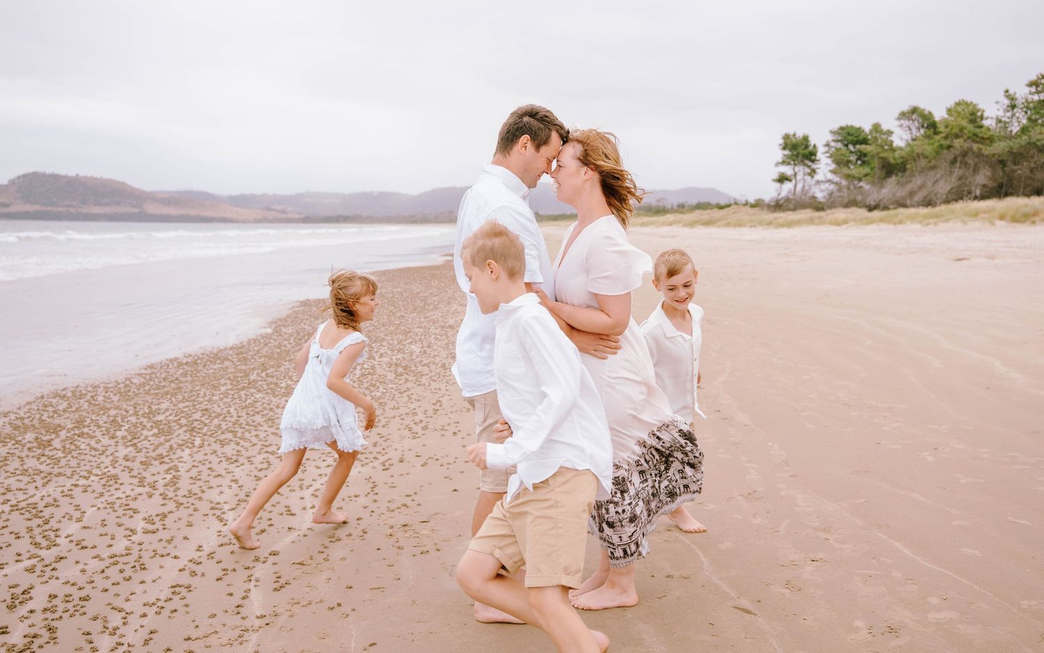 Family in white outfits playing together on a sandy beach during sunset.