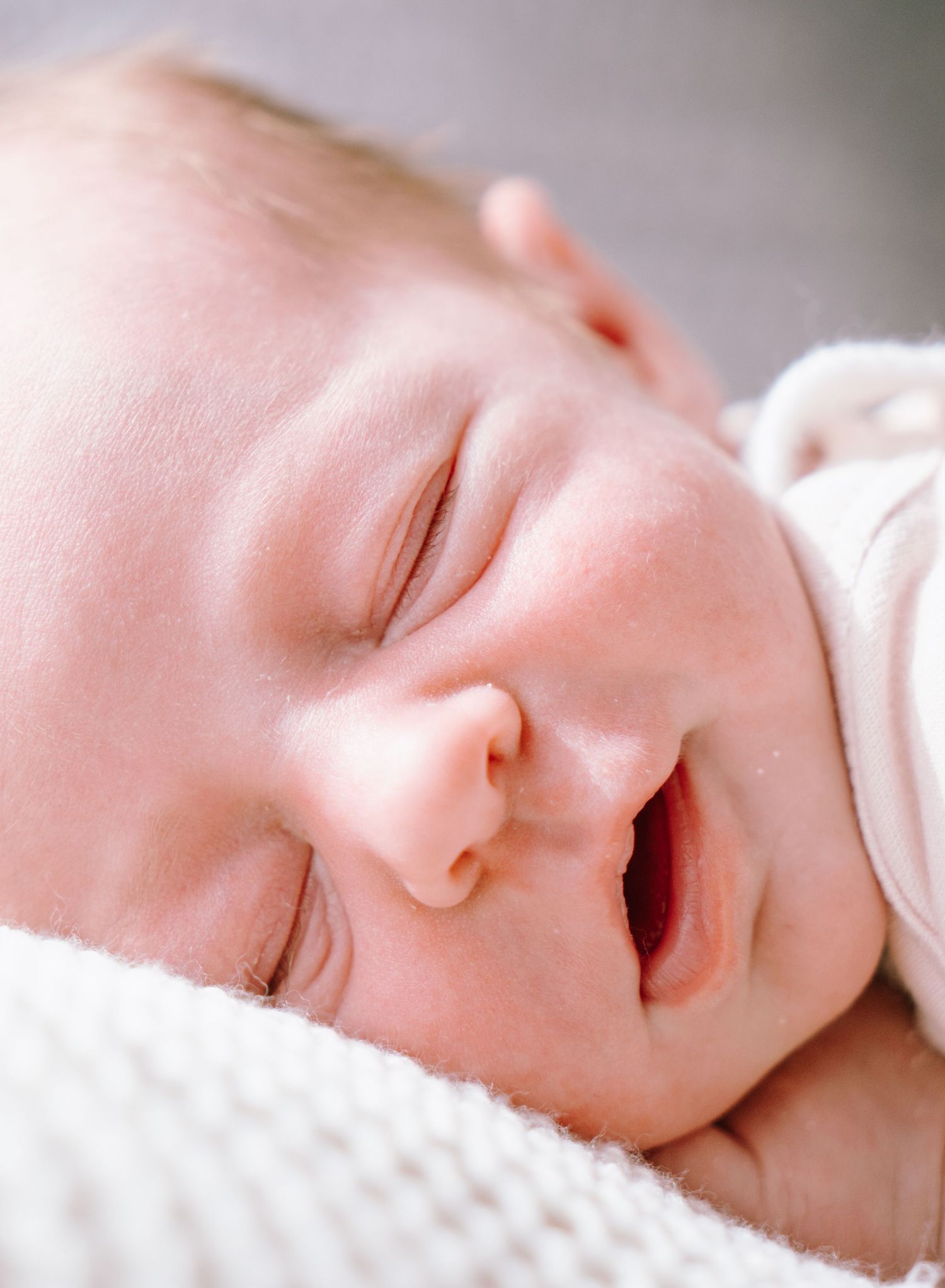 A peaceful sleeping baby wrapped in soft white blankets smiles contentedly while napping.
