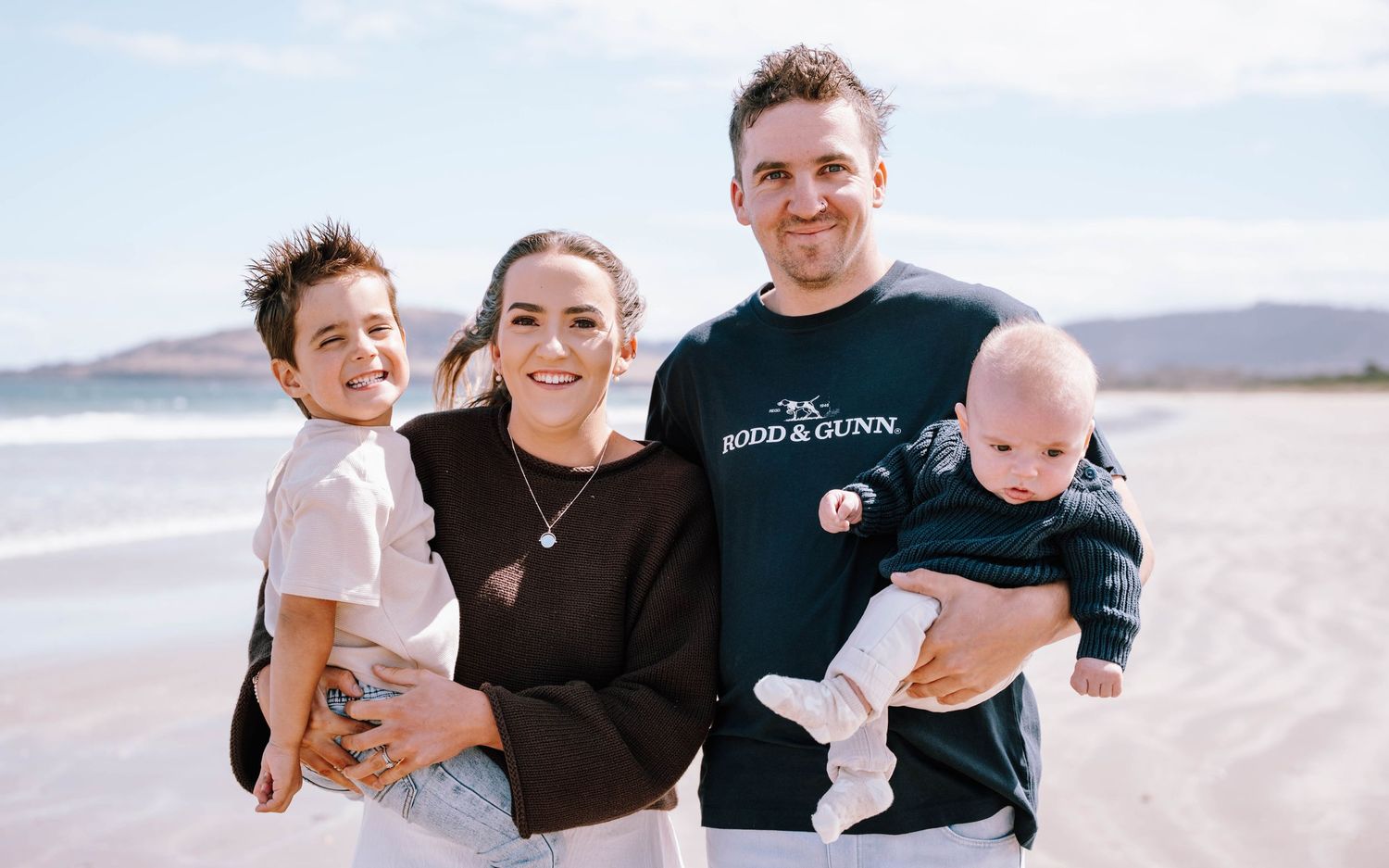 Family group poses together on sandy beach with ocean backdrop.