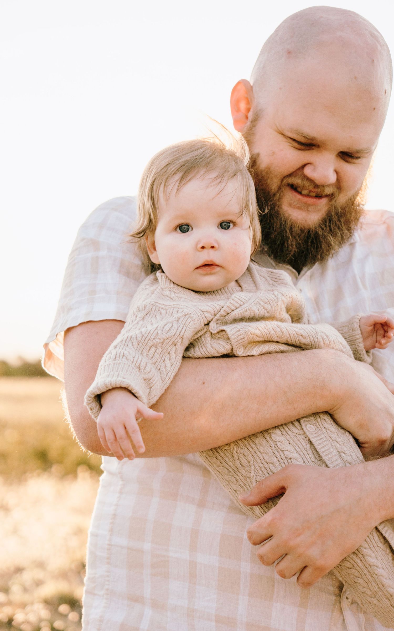 A tender moment between a parent and baby in a knit sweater captured during golden hour in a sunlit field.