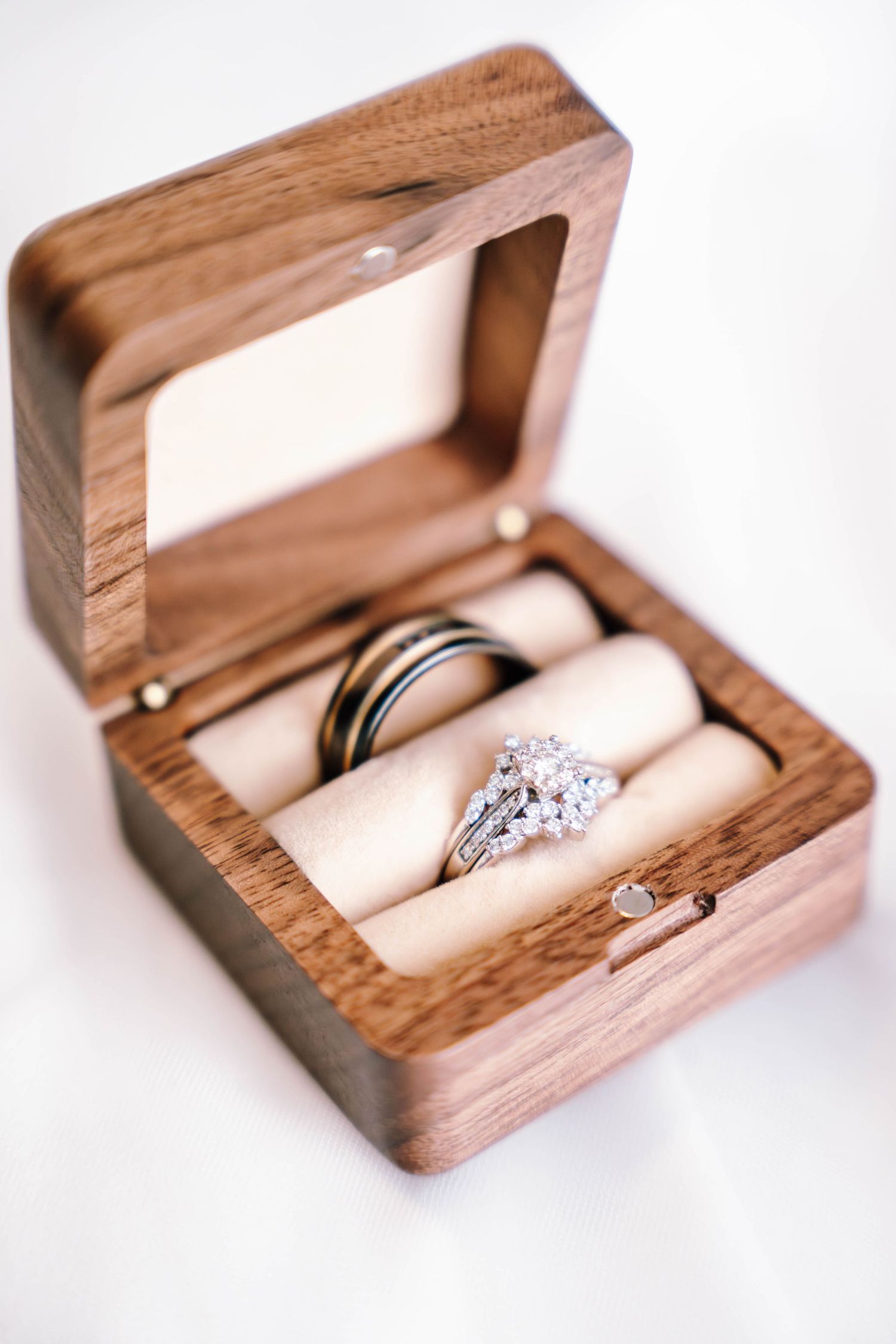 Elegant diamond engagement ring and wedding bands displayed in an open wooden ring box with cream velvet holders.