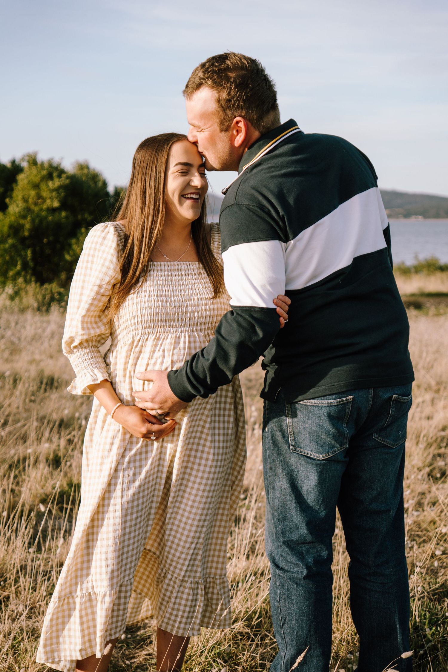 Couple shares tender moments in a sunlit field wearing casual clothing and embracing each other lovingly.