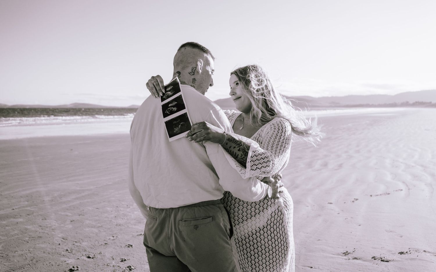 A romantic black and white photo series showing a couple embracing and dancing together on a beach at sunset.