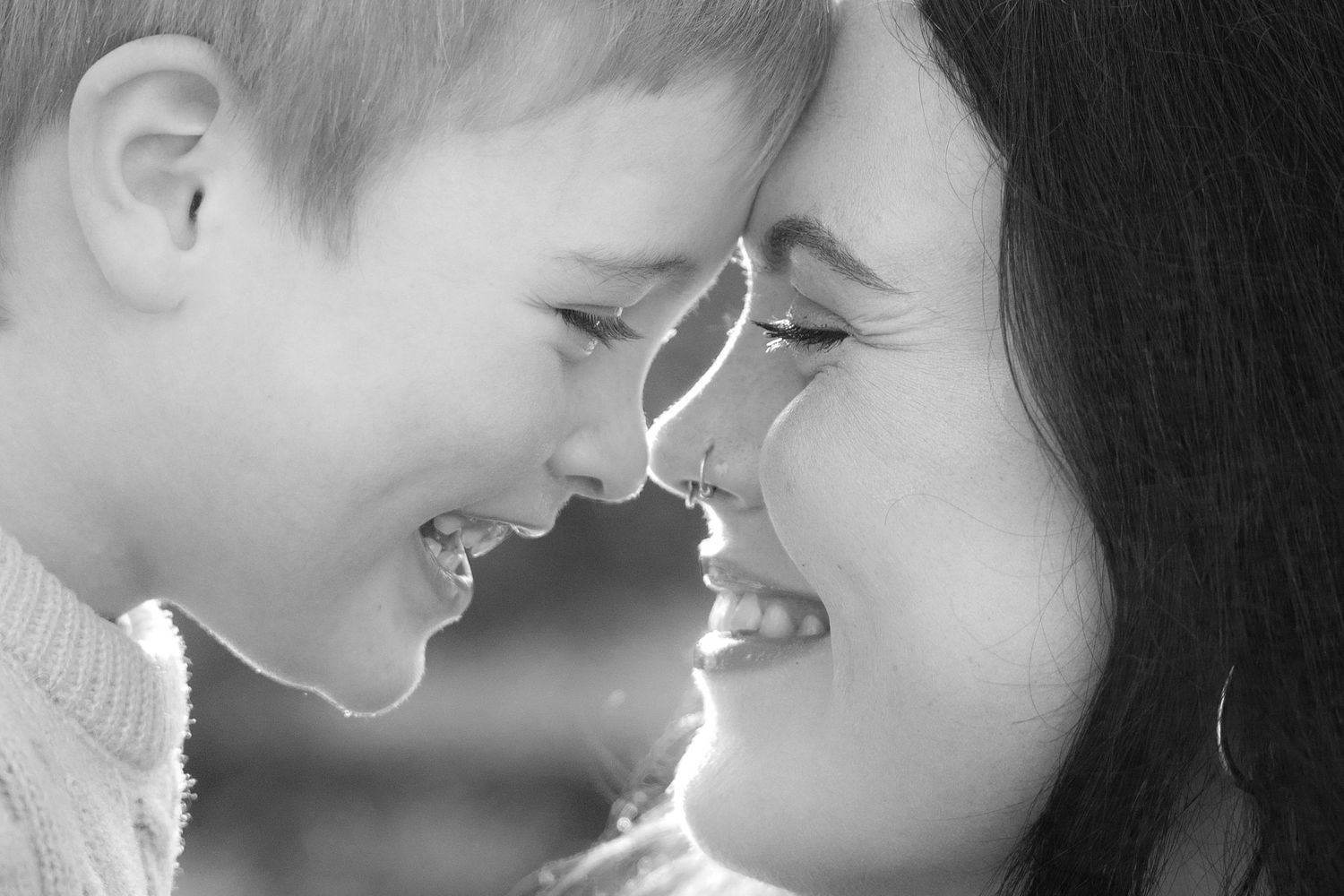 Black and white photo of a mother and young son smiling and touching foreheads in a tender moment.