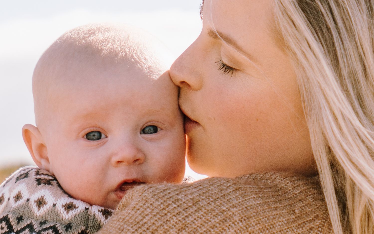 A tender moment between parent and baby as they share a close embrace in warm sunlight.