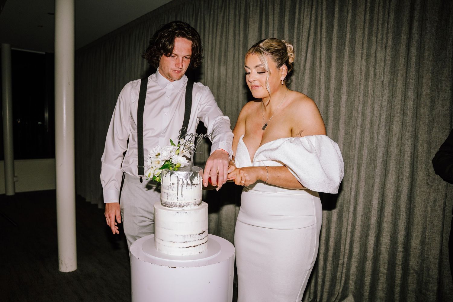 Bride and groom cutting white wedding cake together at reception venue.