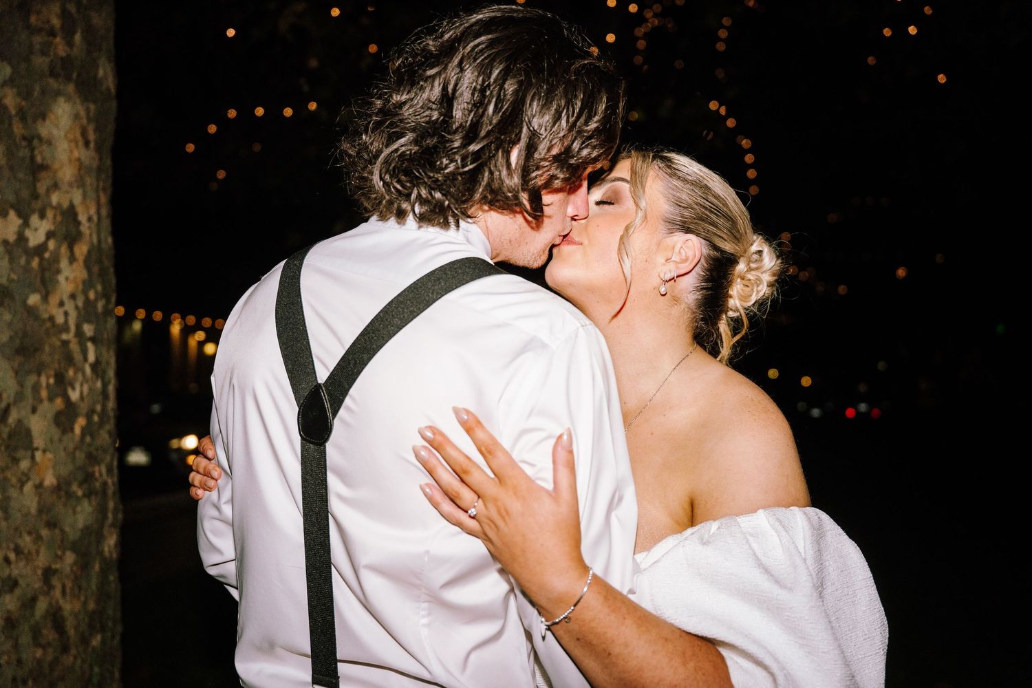 Couple sharing a romantic kiss at night with sparkling bokeh lights in the background at their celebration.