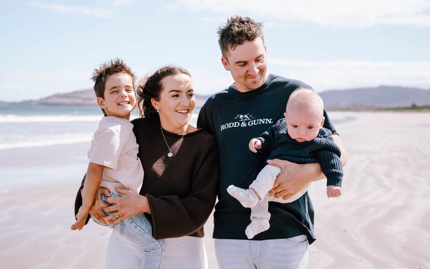 A joyful family plays and laughs together while walking along a scenic beach at sunset.