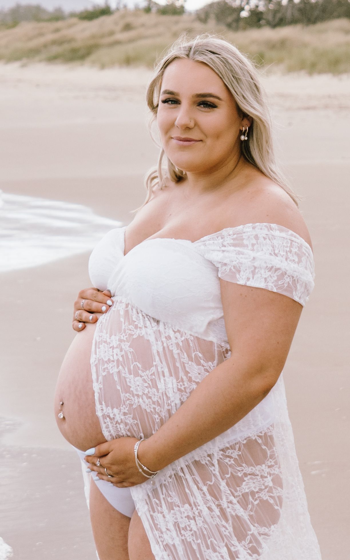 A series of beach maternity photos showing someone in a white lace dress posing against a sandy coastal backdrop.