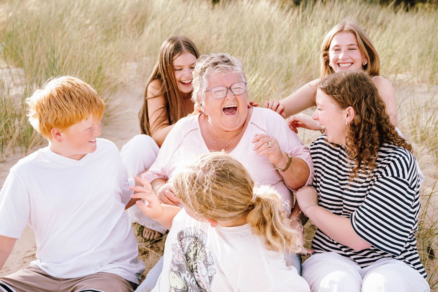 Joyful family gathering on sandy dunes, grandmother laughing with grandchildren around her.