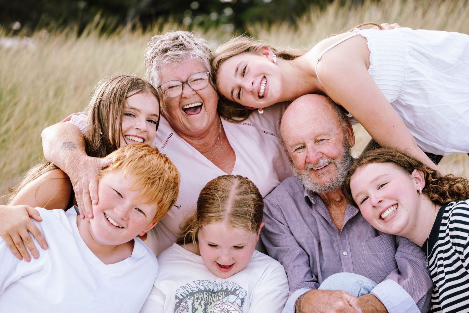 Joyful multigenerational family with grandparents and four grandchildren laughing together outdoors in a golden field.