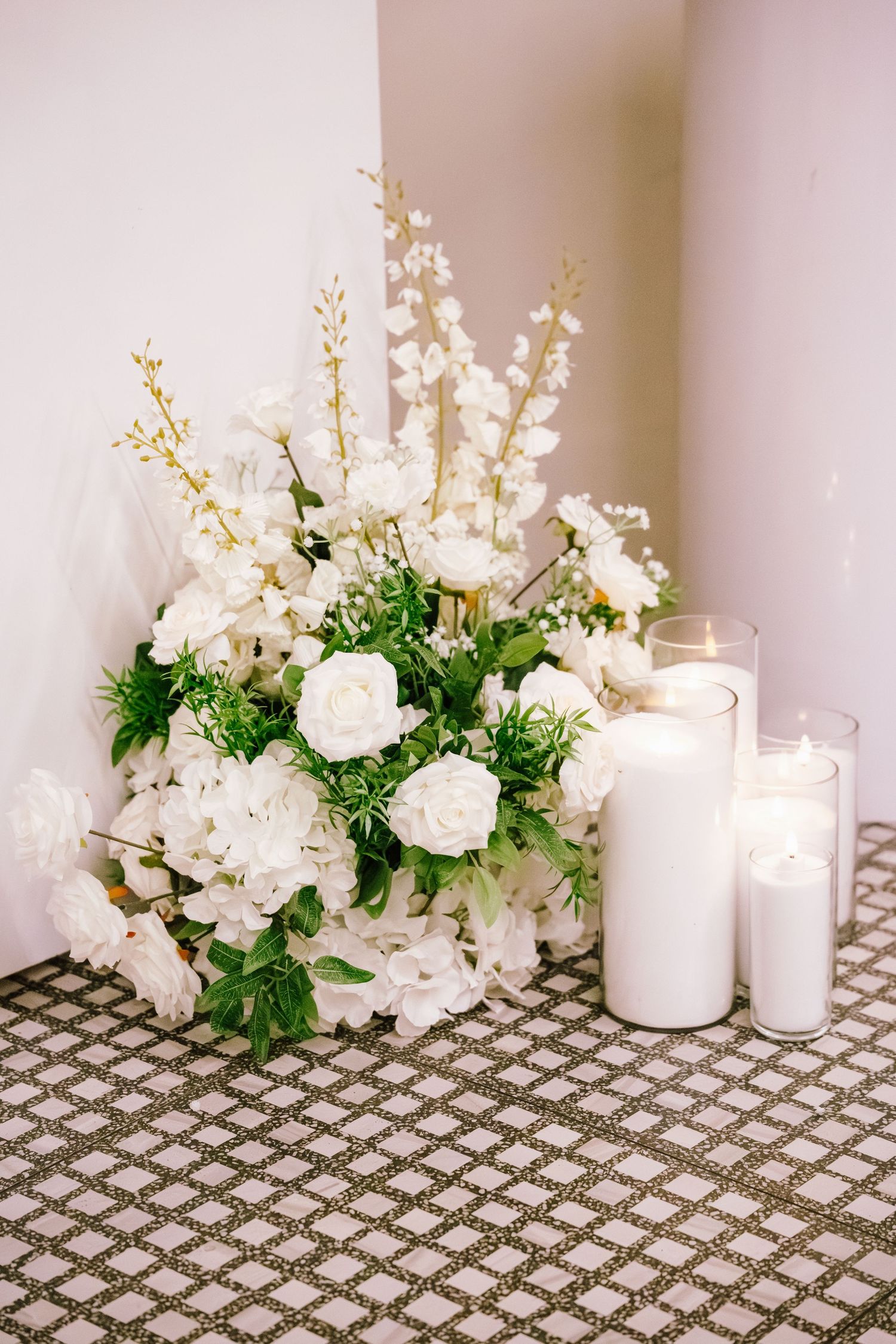 Elegant wedding floral arrangement with white roses and candles on a textured floor.