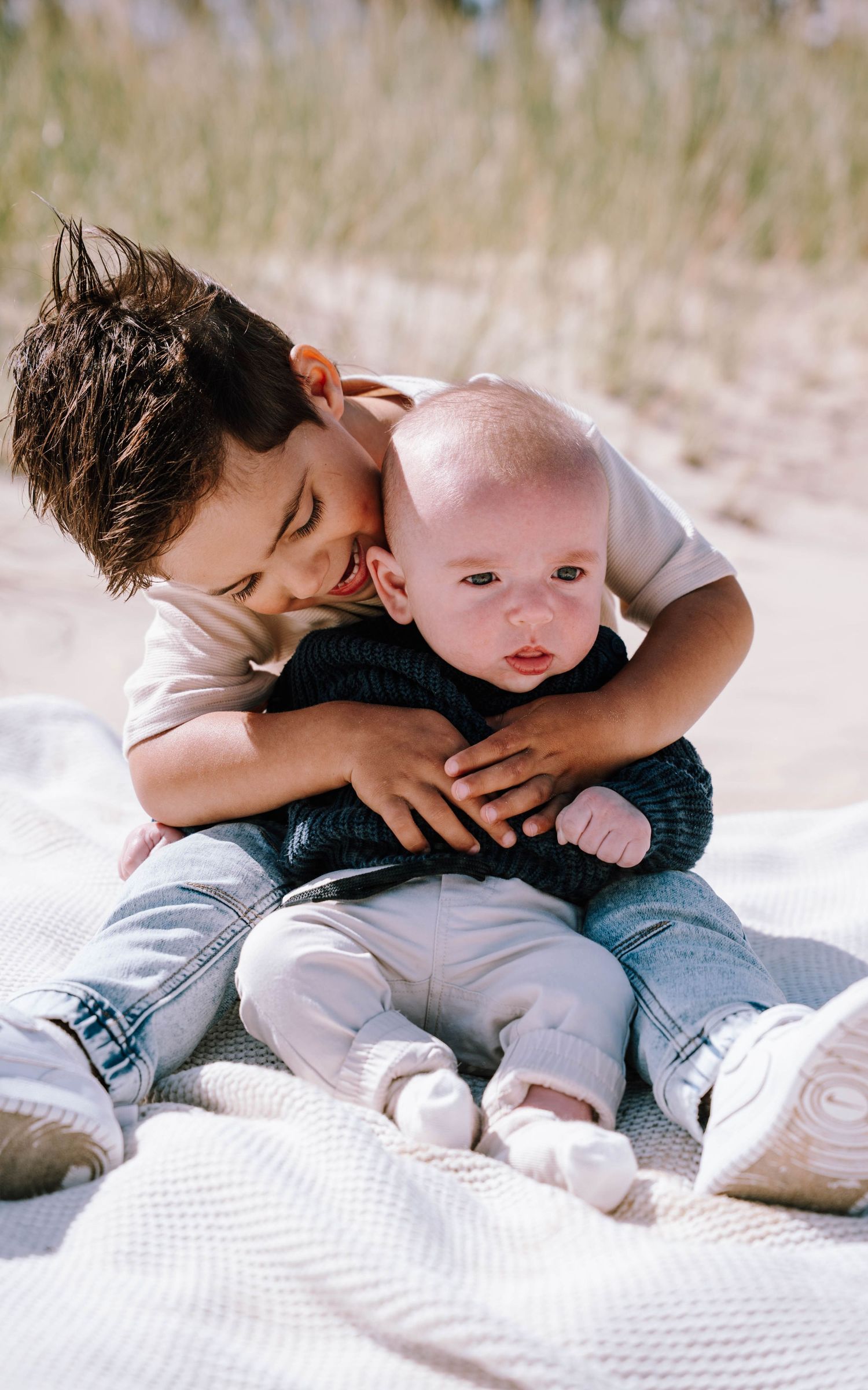 Two siblings sharing sweet moments together while laying on a white blanket in a series of connected photos.