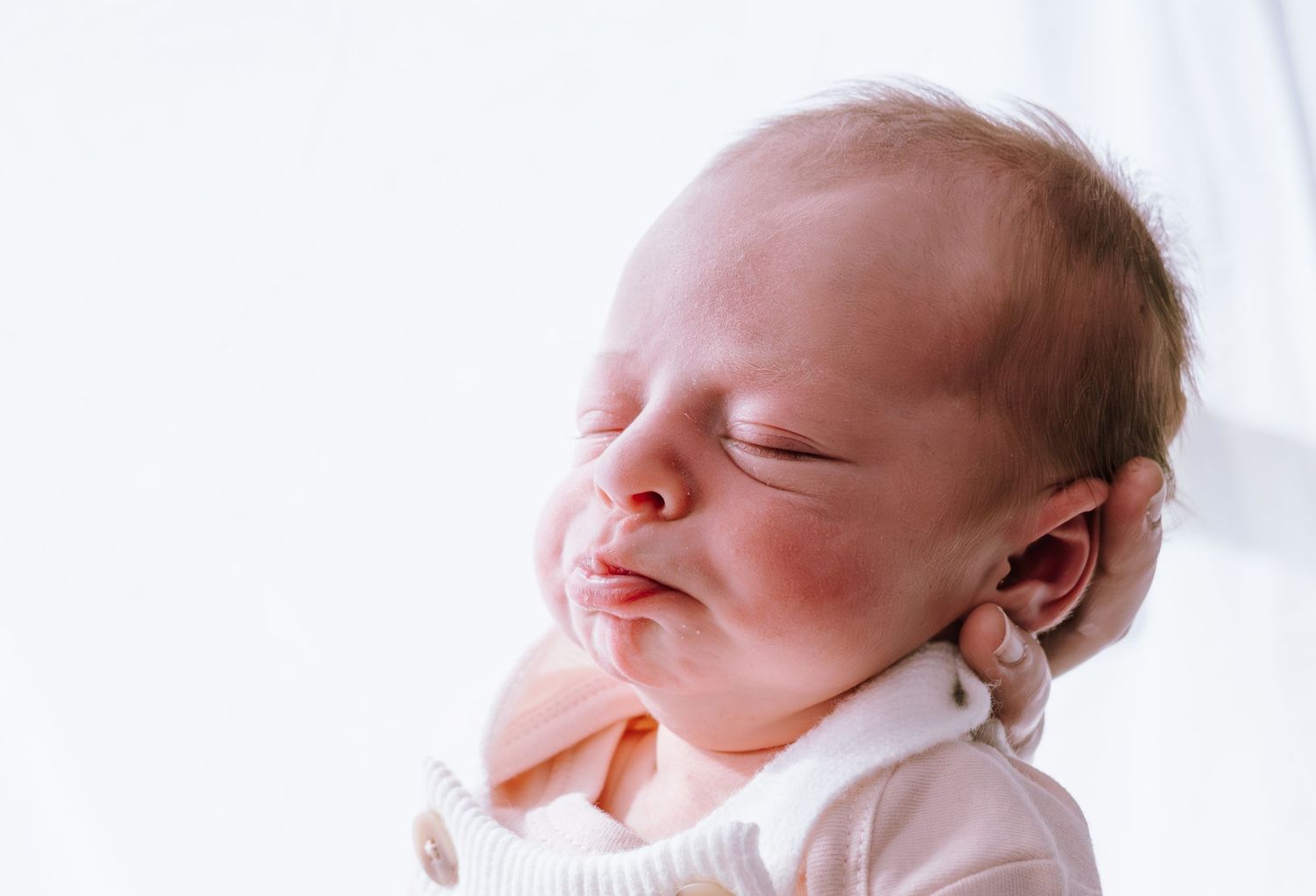 Close-up portrait of sleeping newborn with delicate features against white background.