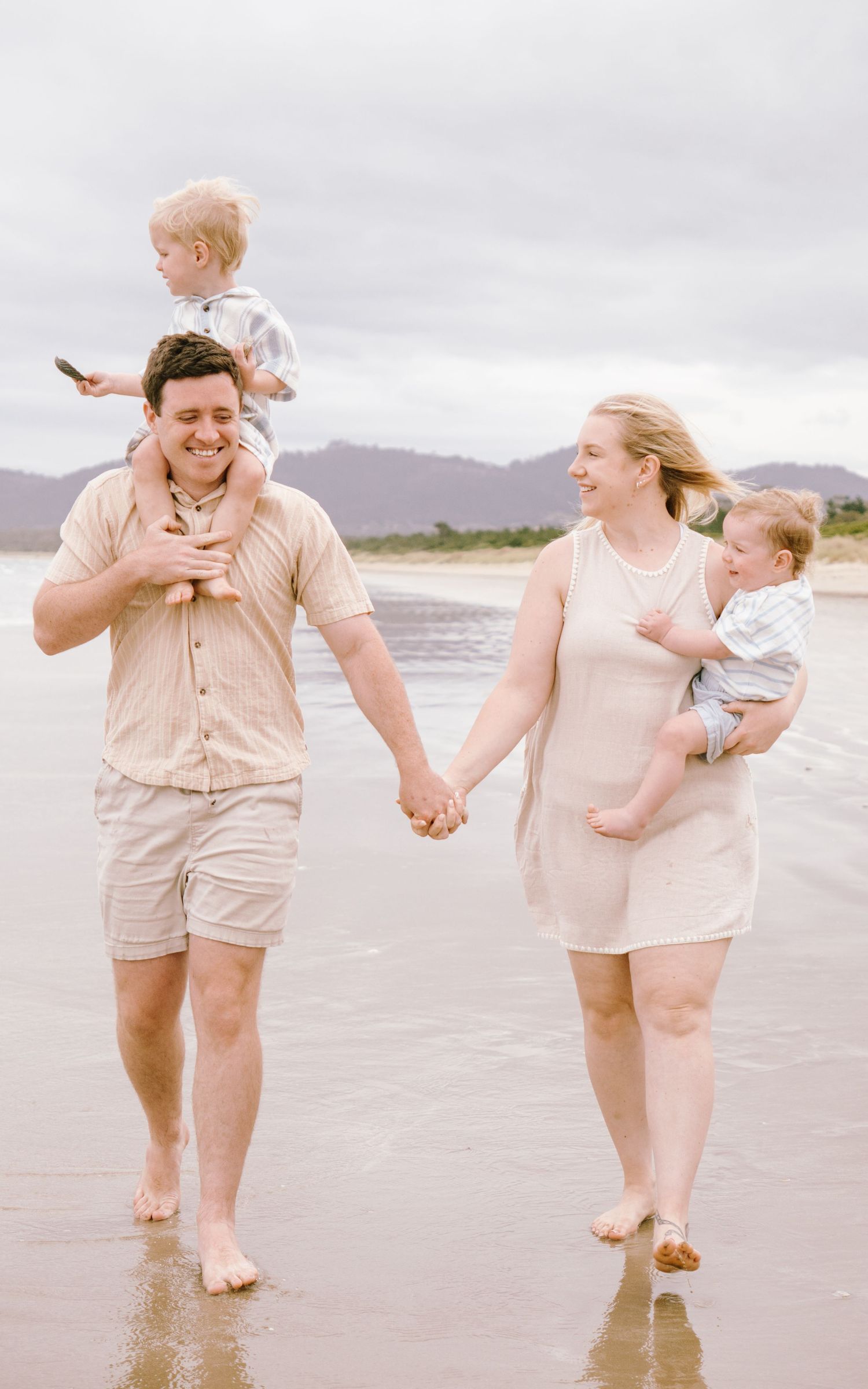 Family walking together and holding hands on a beach with mountains in the background during sunset.