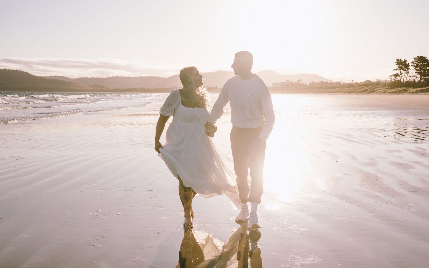 A couple walks together on a sandy beach at sunset creating romantic silhouettes.