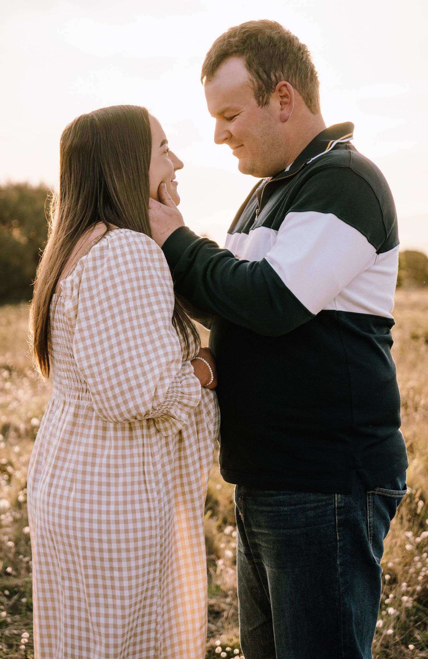 A couple shares a tender moment in a sunlit field wearing casual clothing and embracing.