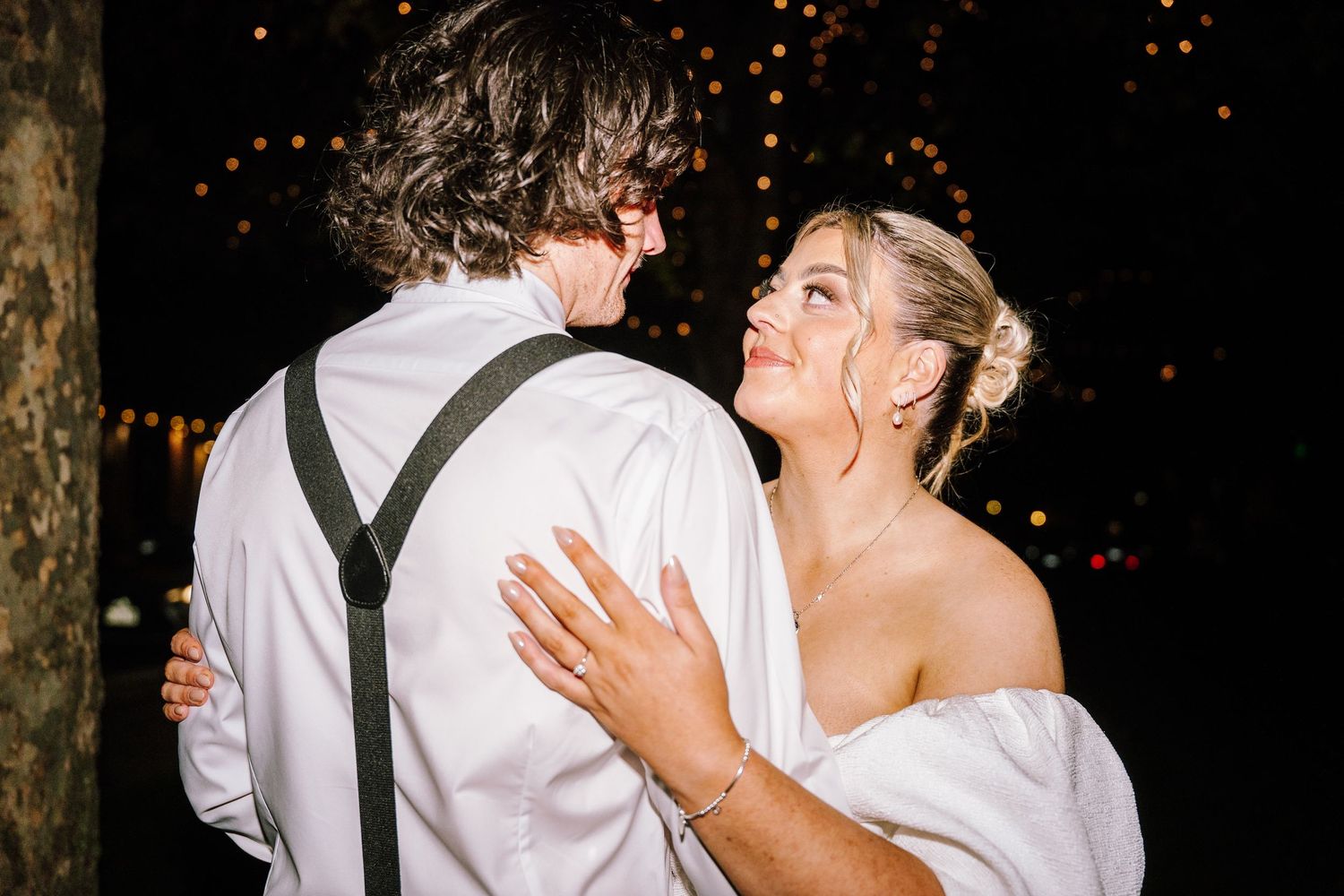 Bride and groom share a romantic first dance outdoors at night, surrounded by warm string lights at their wedding reception.