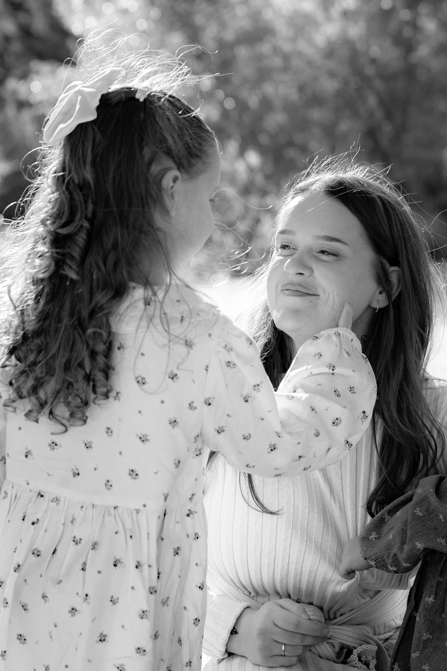 Two girls with long hair share a tender moment outdoors in black and white photo.
