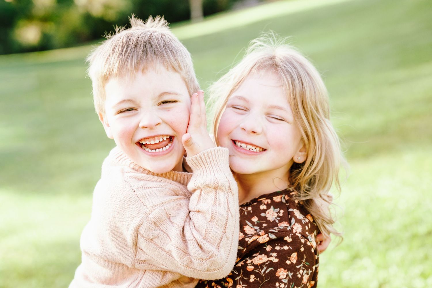 Two happy children laughing and hugging outdoors in a sunny green park, a boy and girl sharing a joyful moment.