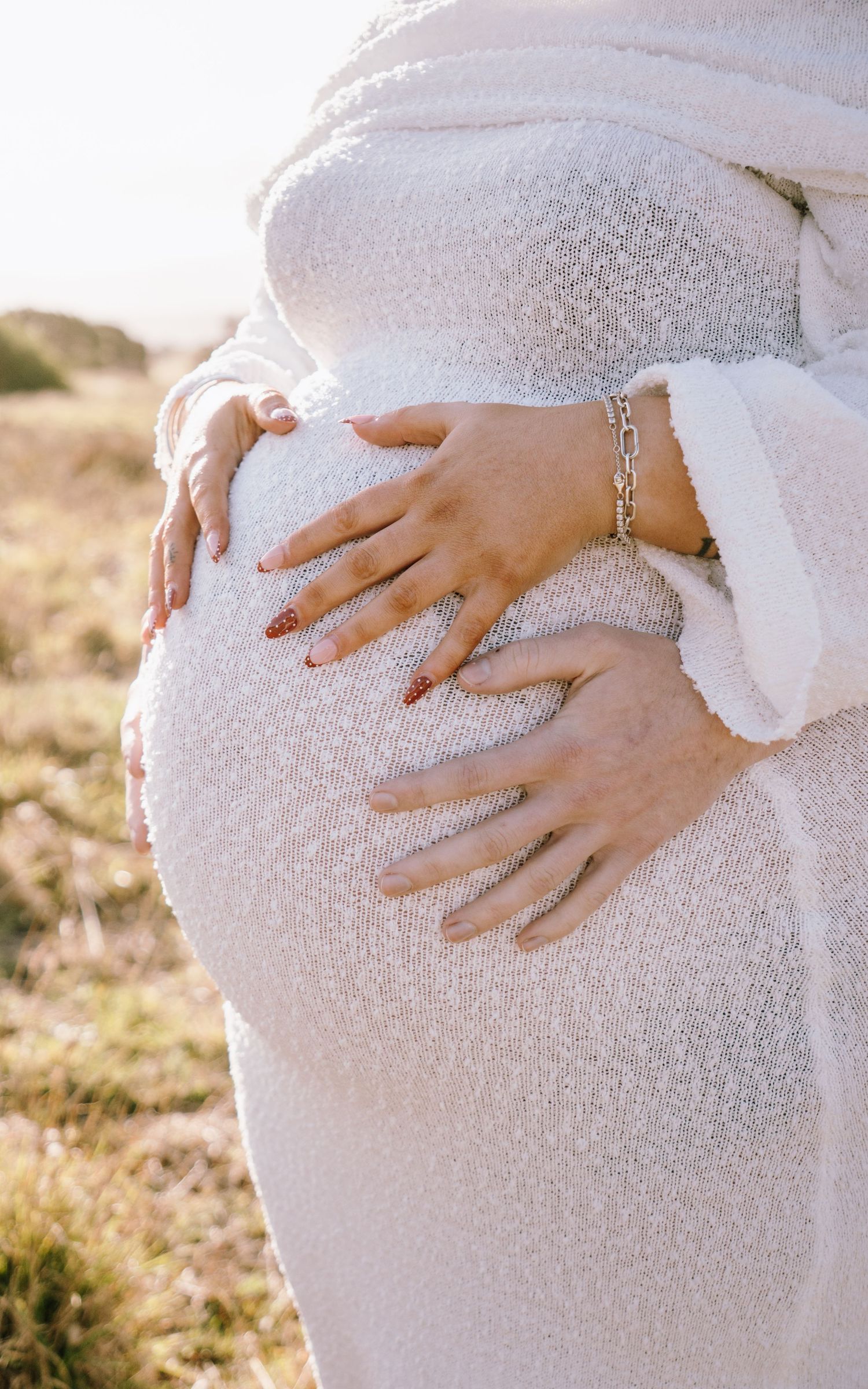 Close-up shot of hands gently cradling a pregnant belly in white lace dress during golden hour maternity photoshoot.