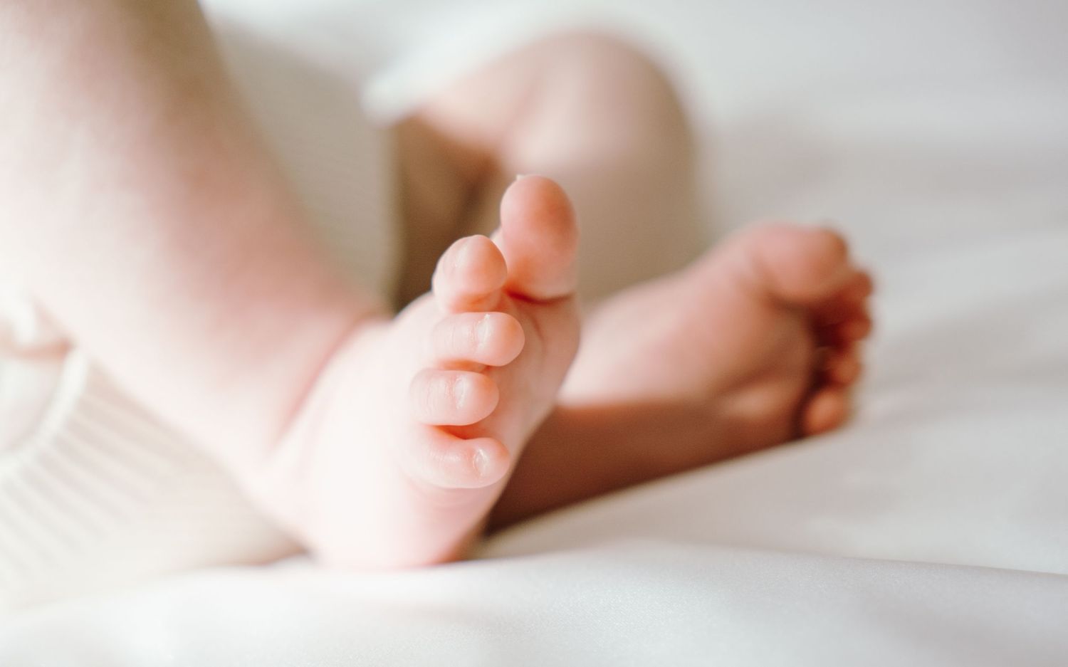 Close-up of tiny baby feet resting on soft white bedding in natural light.