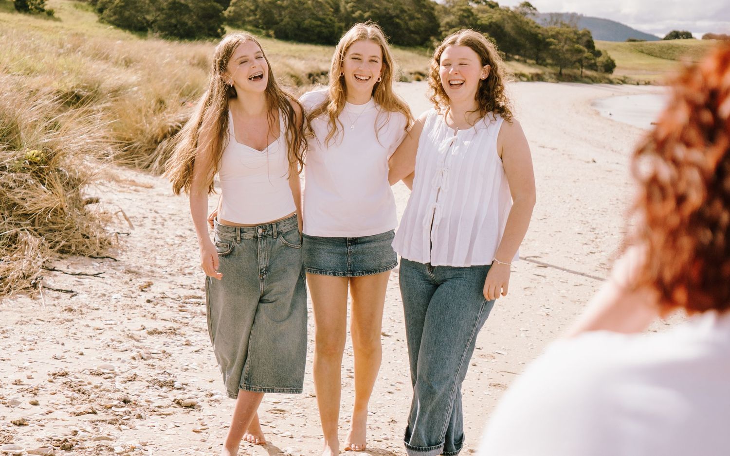 Group of friends walking together on a sandy beach path during a bright sunny day.