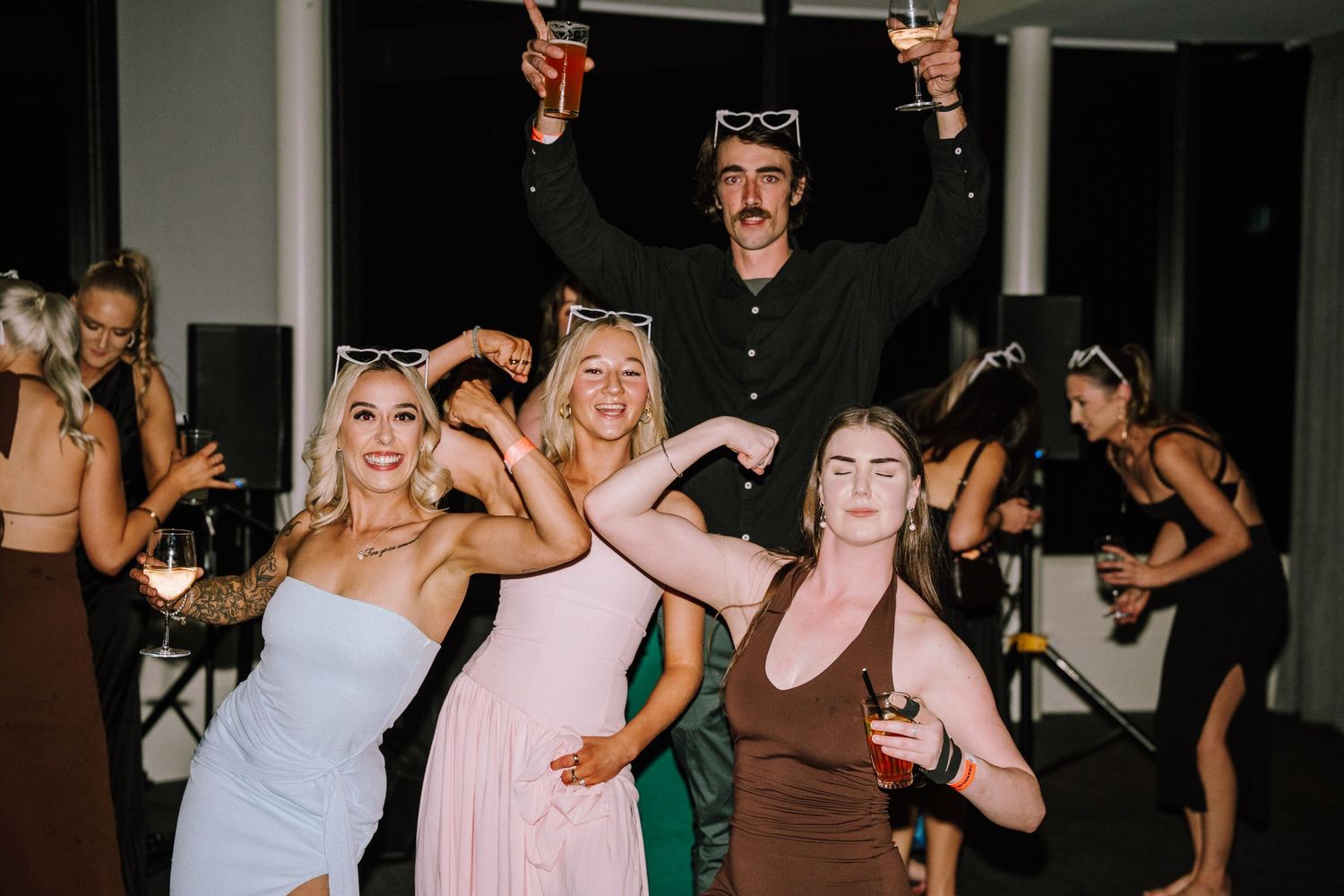 Group of friends dancing and celebrating at a wedding reception party, raising drinks and smiling.