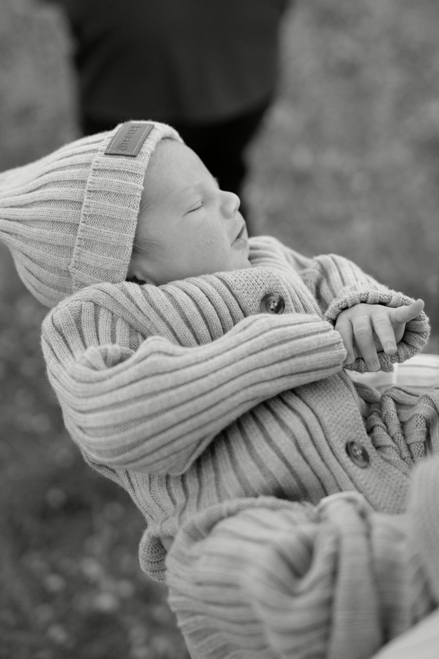 Sleeping newborn baby in knit outfit and hat, peaceful close-up black and white photo.
