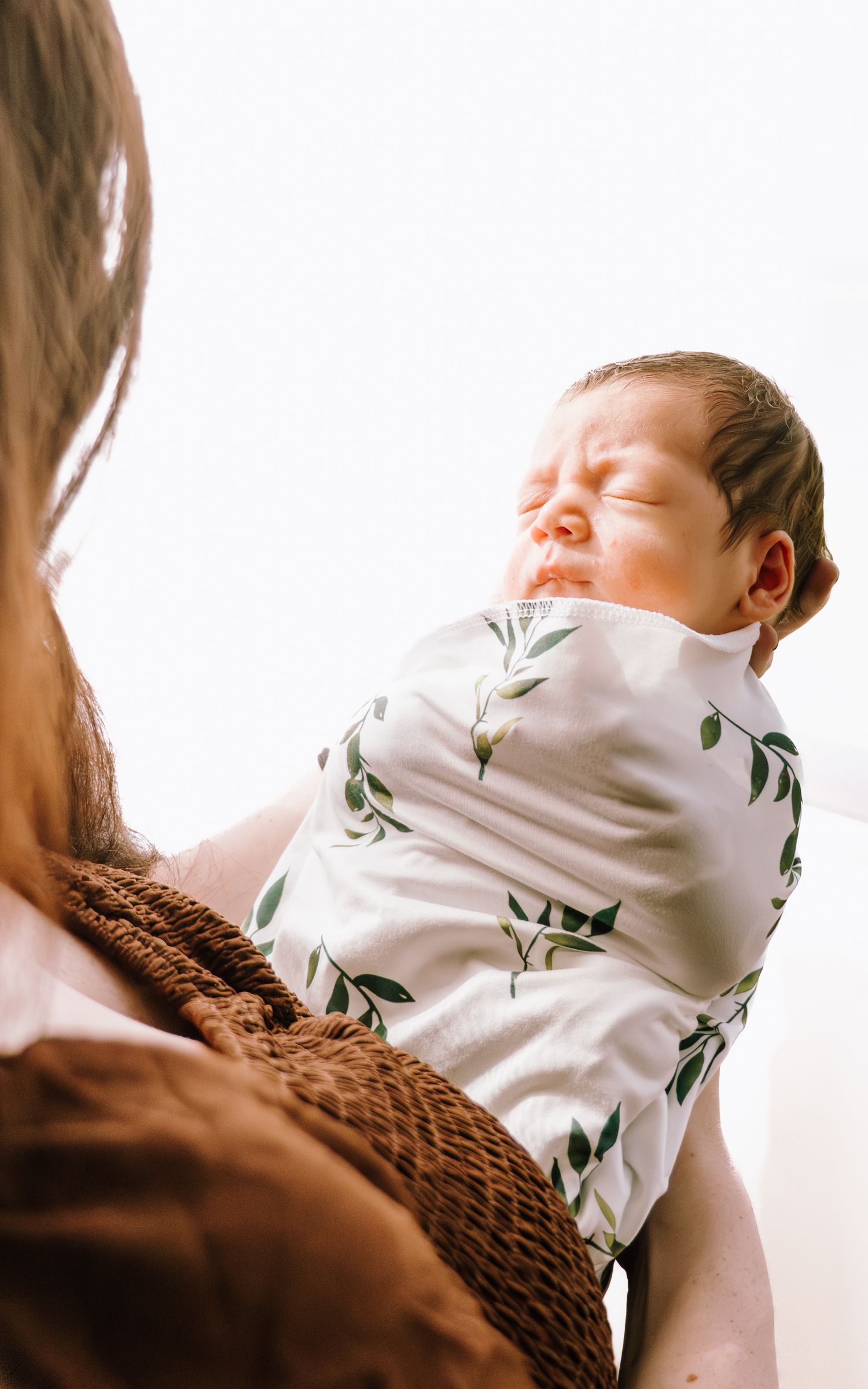 A baby in a white floral onesie rests peacefully in a brown woven basket while sleeping.