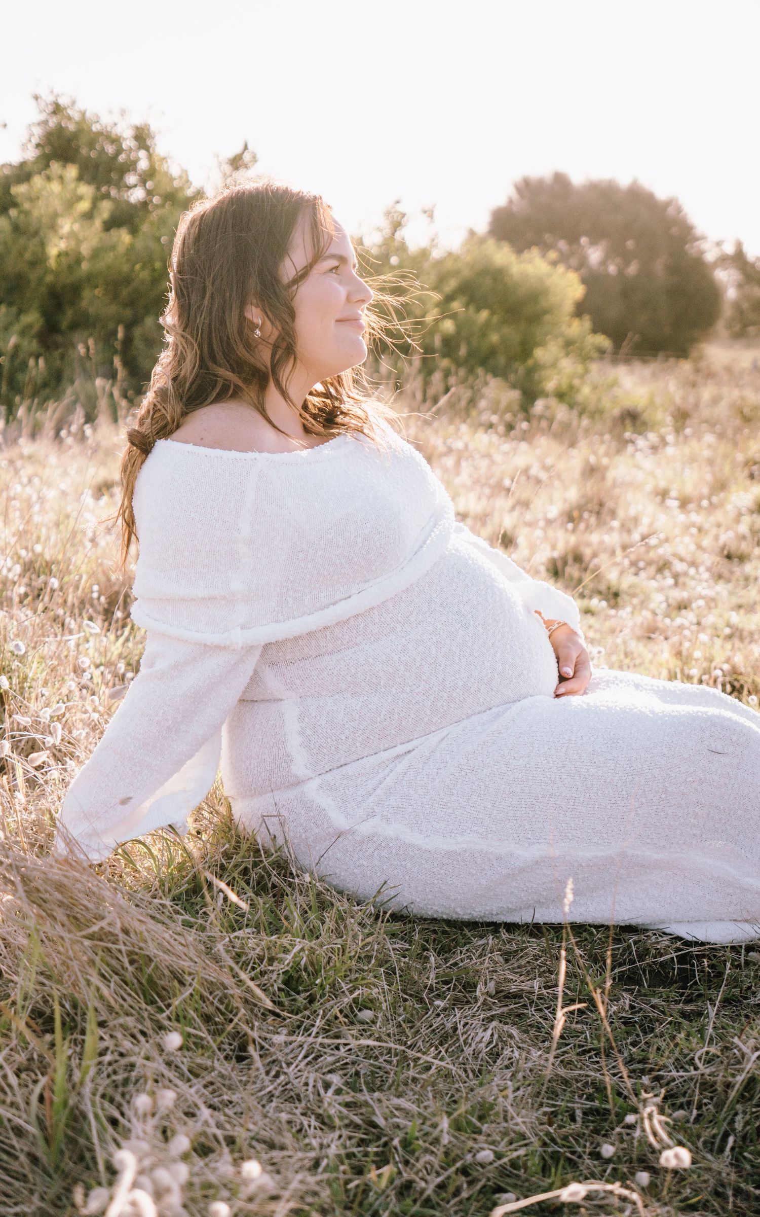 Person wrapped in white blanket lying in golden sunlit grass during sunset creating dreamy outdoor portrait.