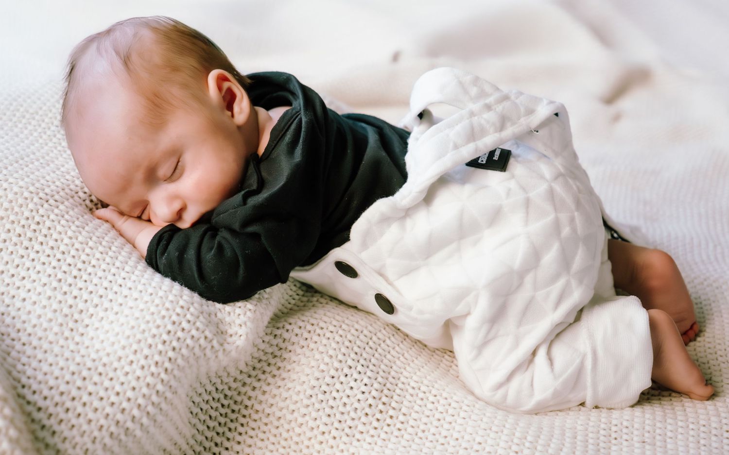 A sleeping baby in white clothing lies peacefully on textured bedding in a series of connected photos.