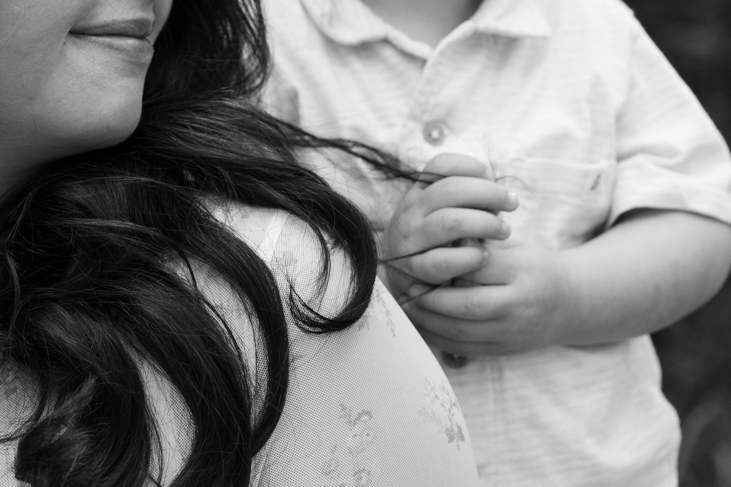 Black and white close-up of a toddlers hand touching a pregnant mothers belly.