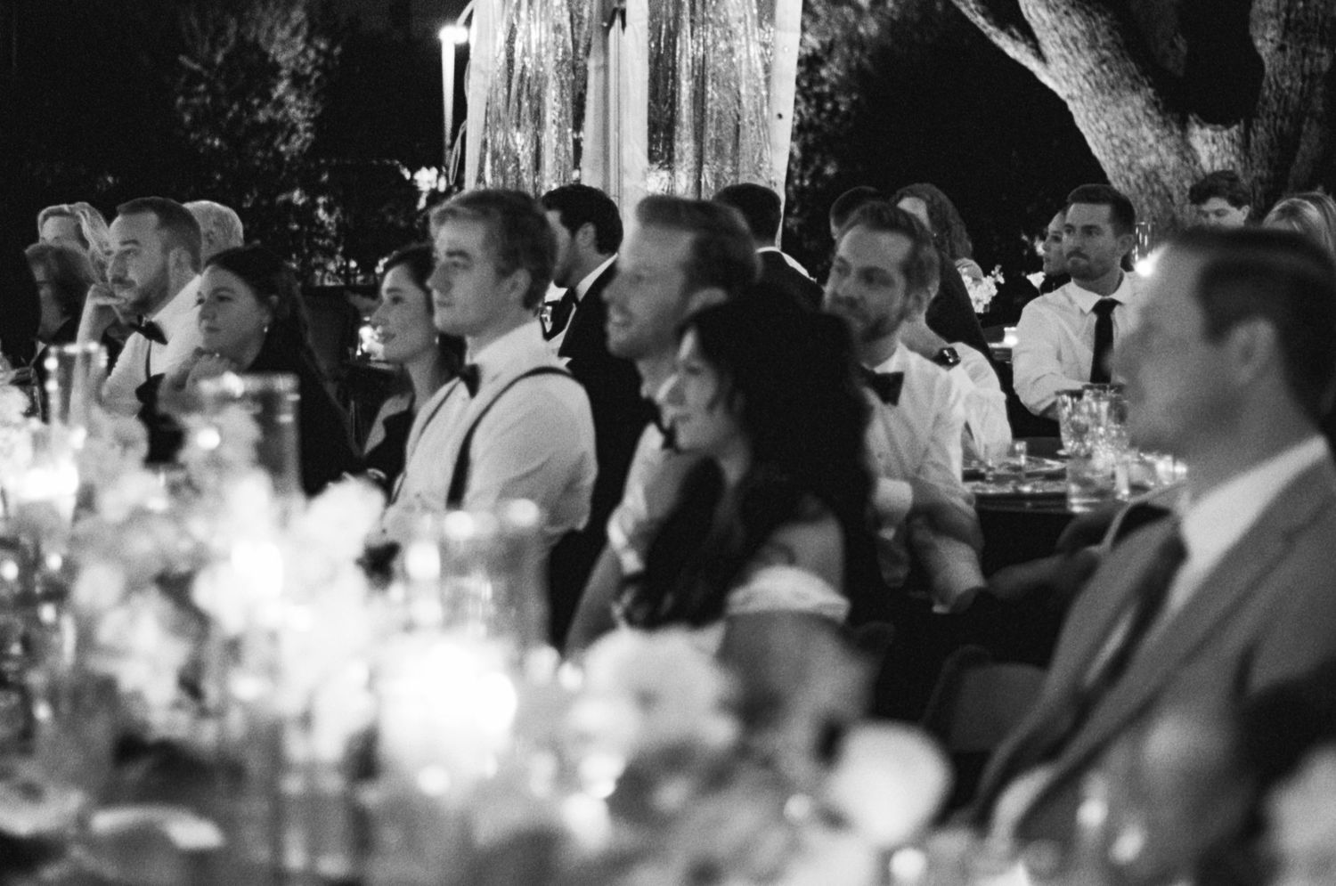 Black and white photo of wedding reception guests seated at tables laughing and enjoying the celebration.