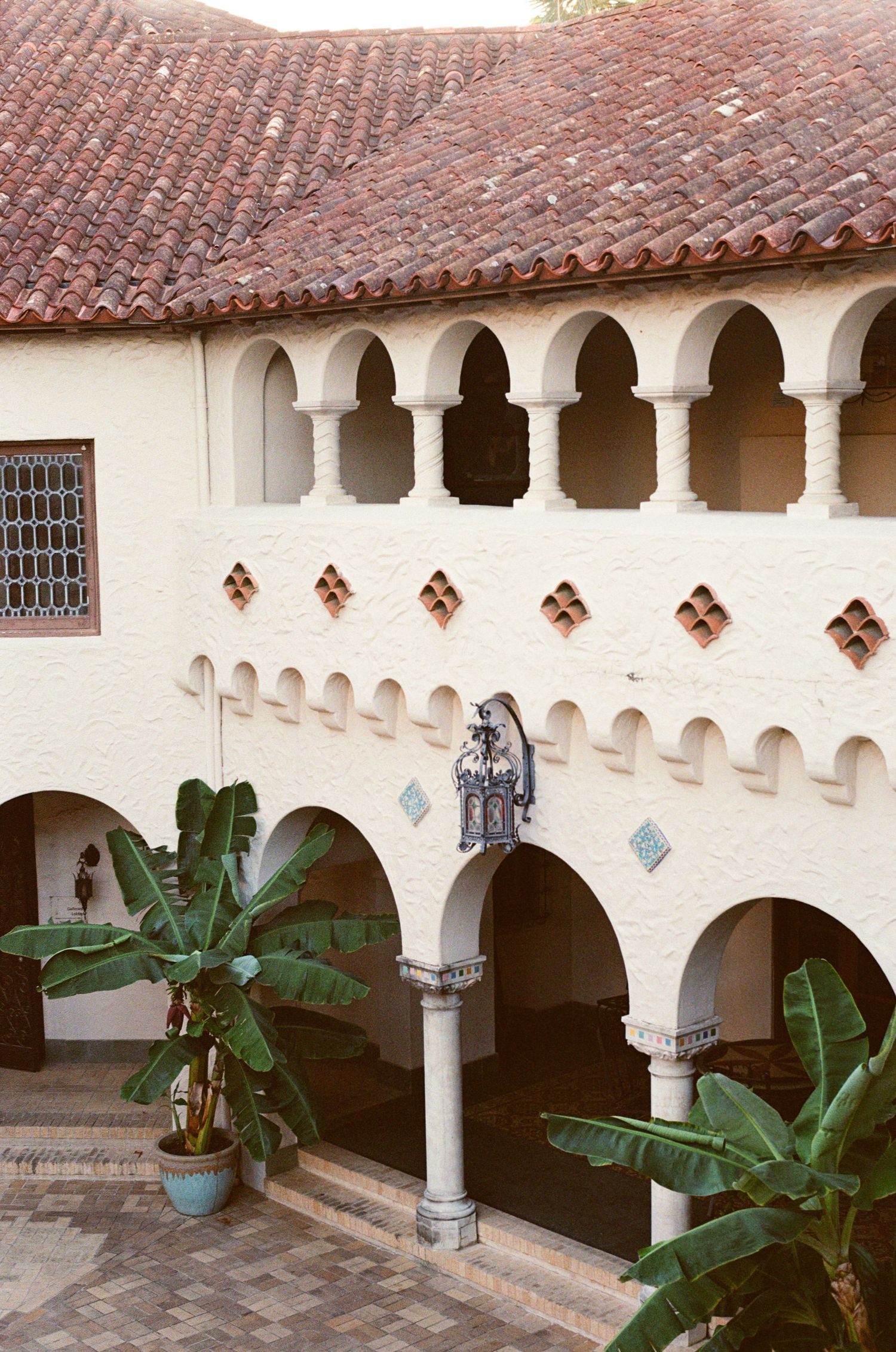 Spanish Colonial Revival architecture with arched colonnades, terracotta roof tiles, and tropical banana plants.