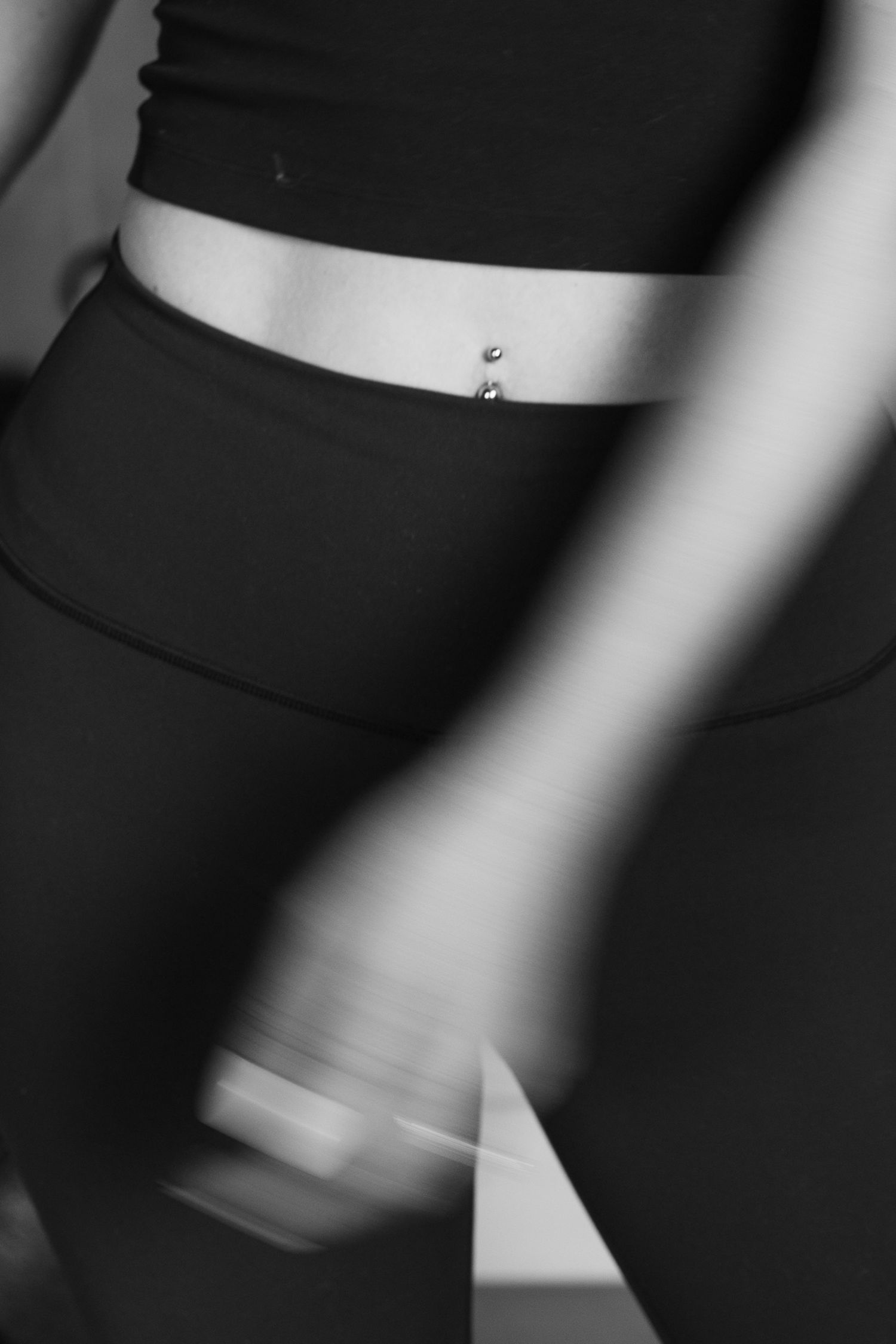 Black and white blurred photo of woman in crop top with belly button piercing.