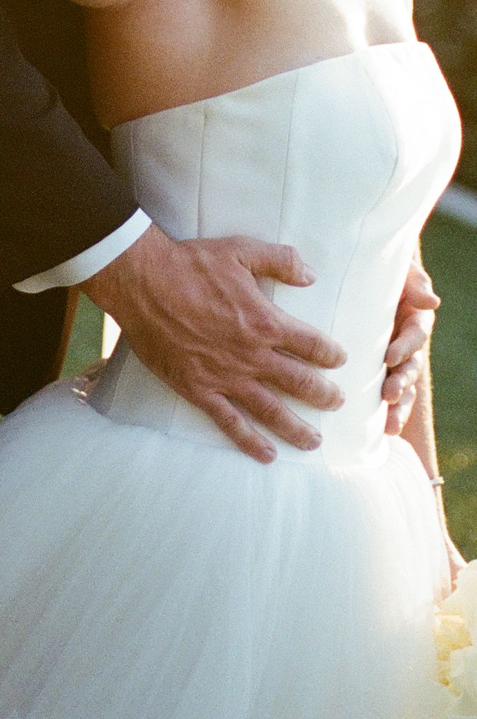Close-up of groom's hand around bride's waist in a strapless white tulle wedding gown.